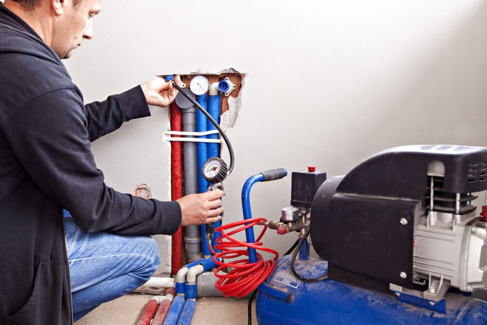 Man Working on A Plumbing System with An Air Compressor — Professional Plumber in Toowoomba