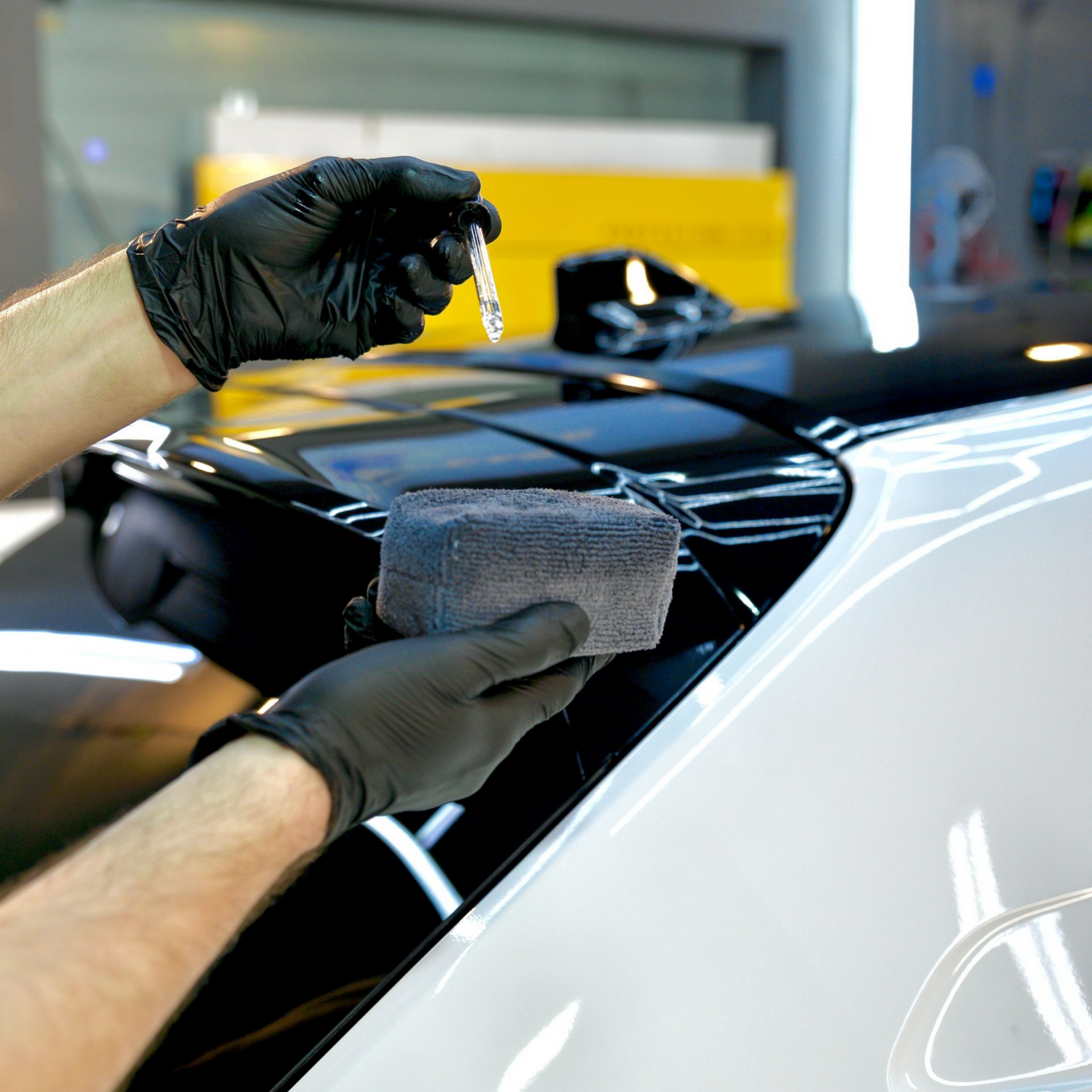 Person in black gloves applying ceramic coating to a car's surface with an applicator sponge.