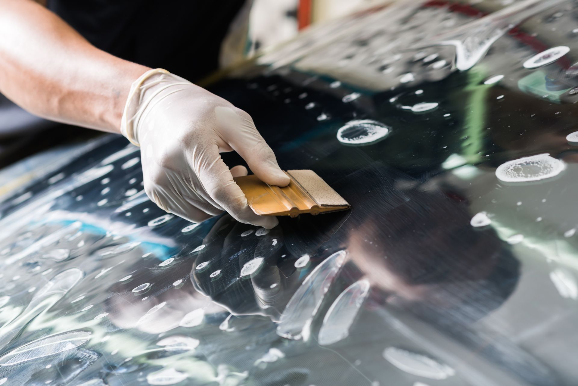 Gloved hand using a squeegee to apply tinted film to a surface, removing bubbles.