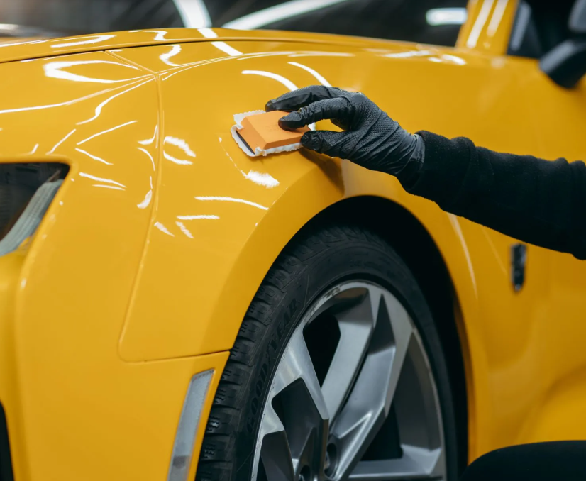 Hand polishing a yellow sports car’s front fender with a sponge
