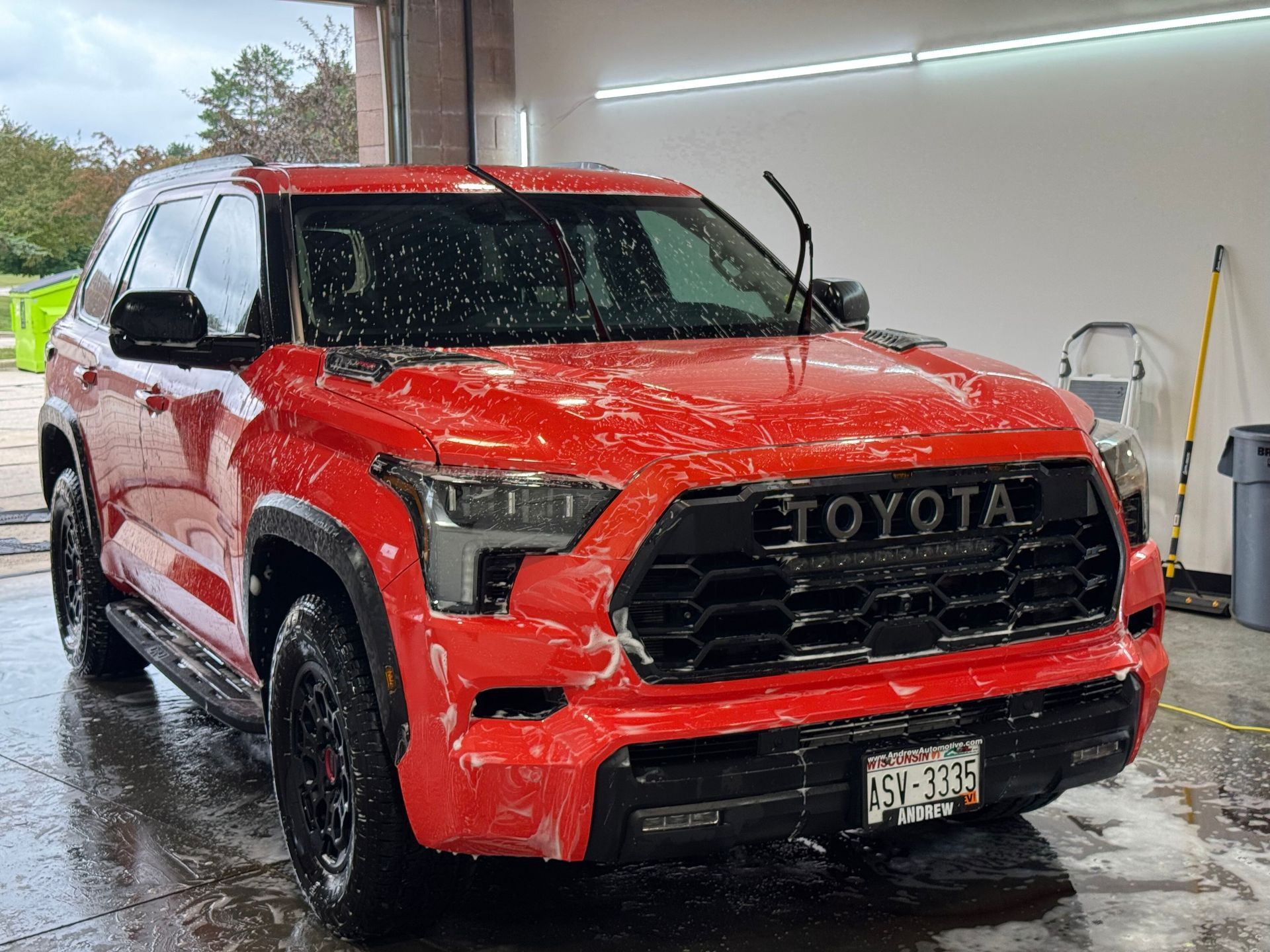 Red Toyota SUV being washed under a carport, covered in water and soap.