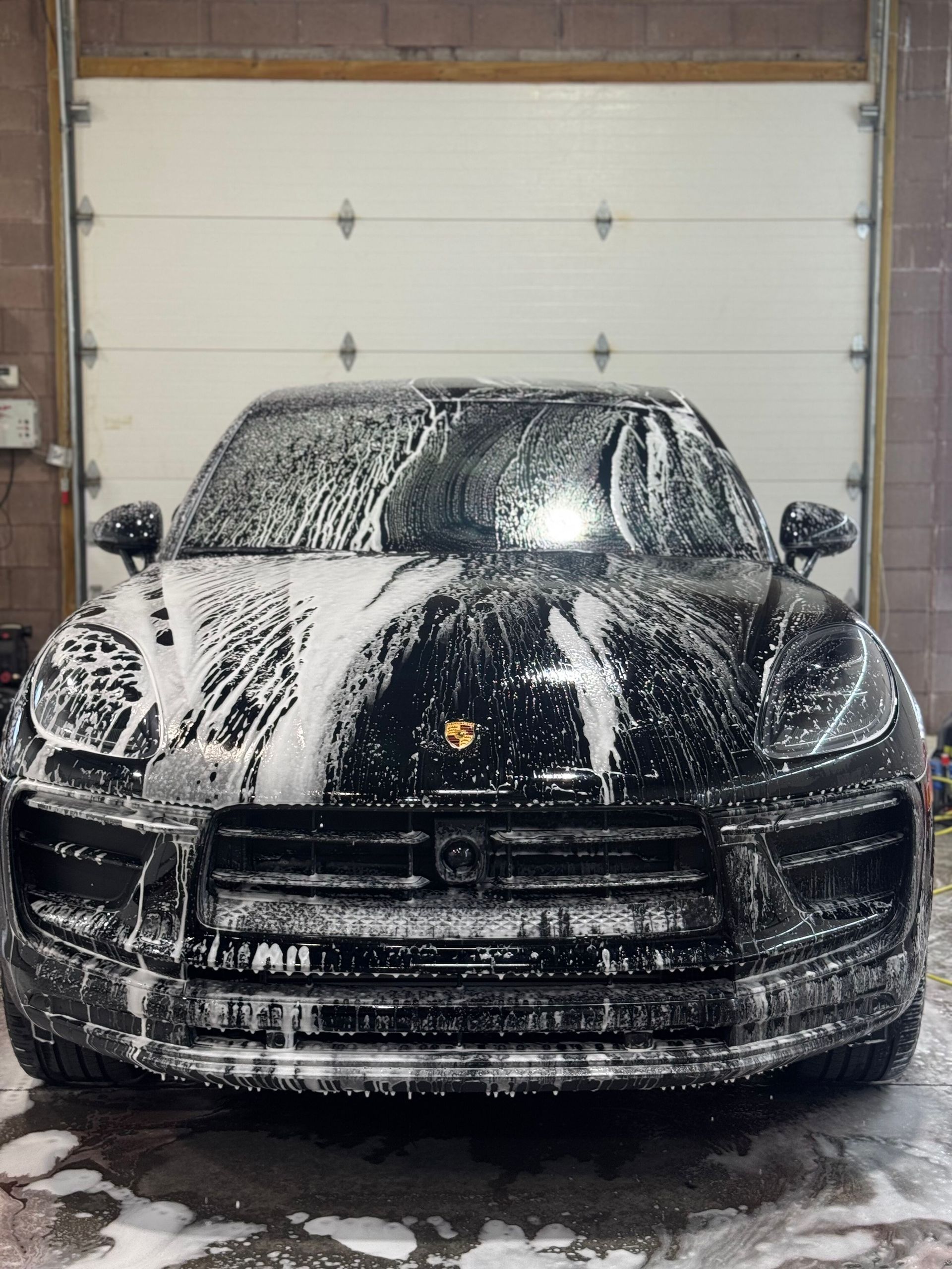Black sports car covered in foam during a wash inside a garage.