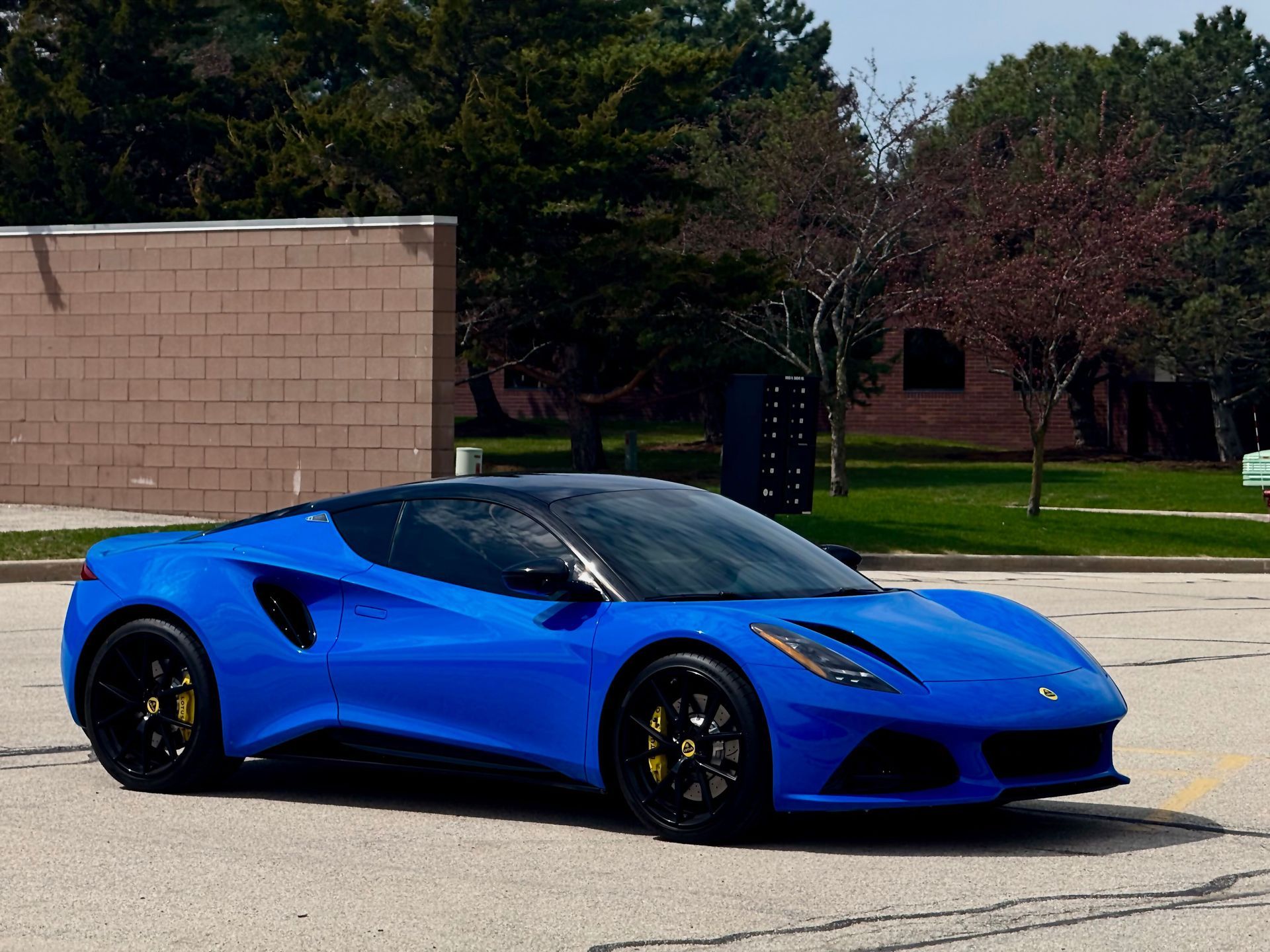 Blue sports car parked outdoors on a sunny day with trees and a building in the background