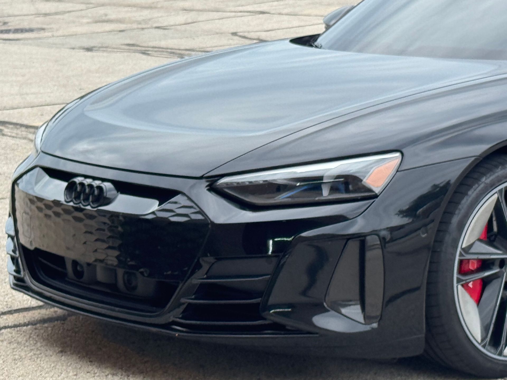 Black Audi sedan front end, close-up on hood, grille, and headlight with red brake caliper visible.