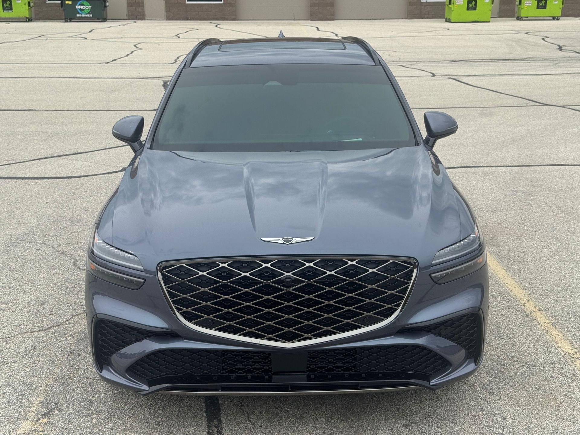 Gray Genesis GV70 SUV from a front-facing perspective, parked outside. Black grill, tinted windows, and gray paint.