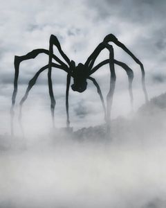 A giant spider is standing in the fog on top of a hill.