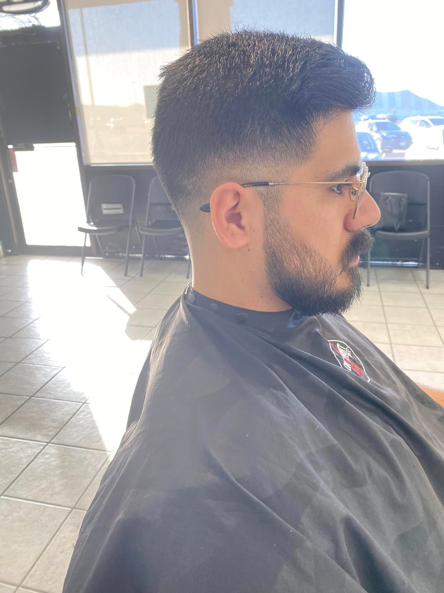 Profile view of a man getting a haircut in a barber chair, wearing glasses and a dark cape.