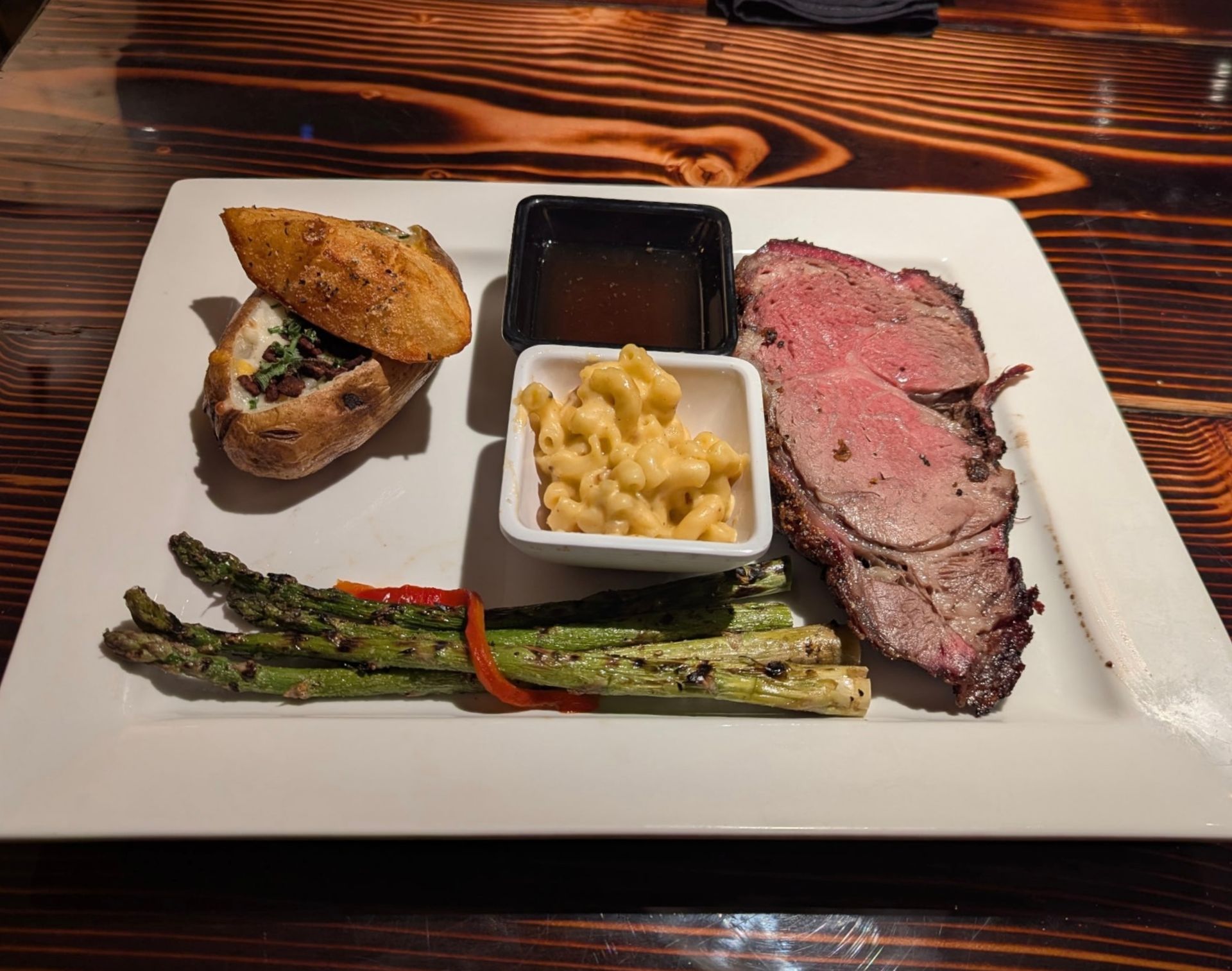 Plated steak dinner with asparagus, macaroni and cheese, and bread on a white square plate