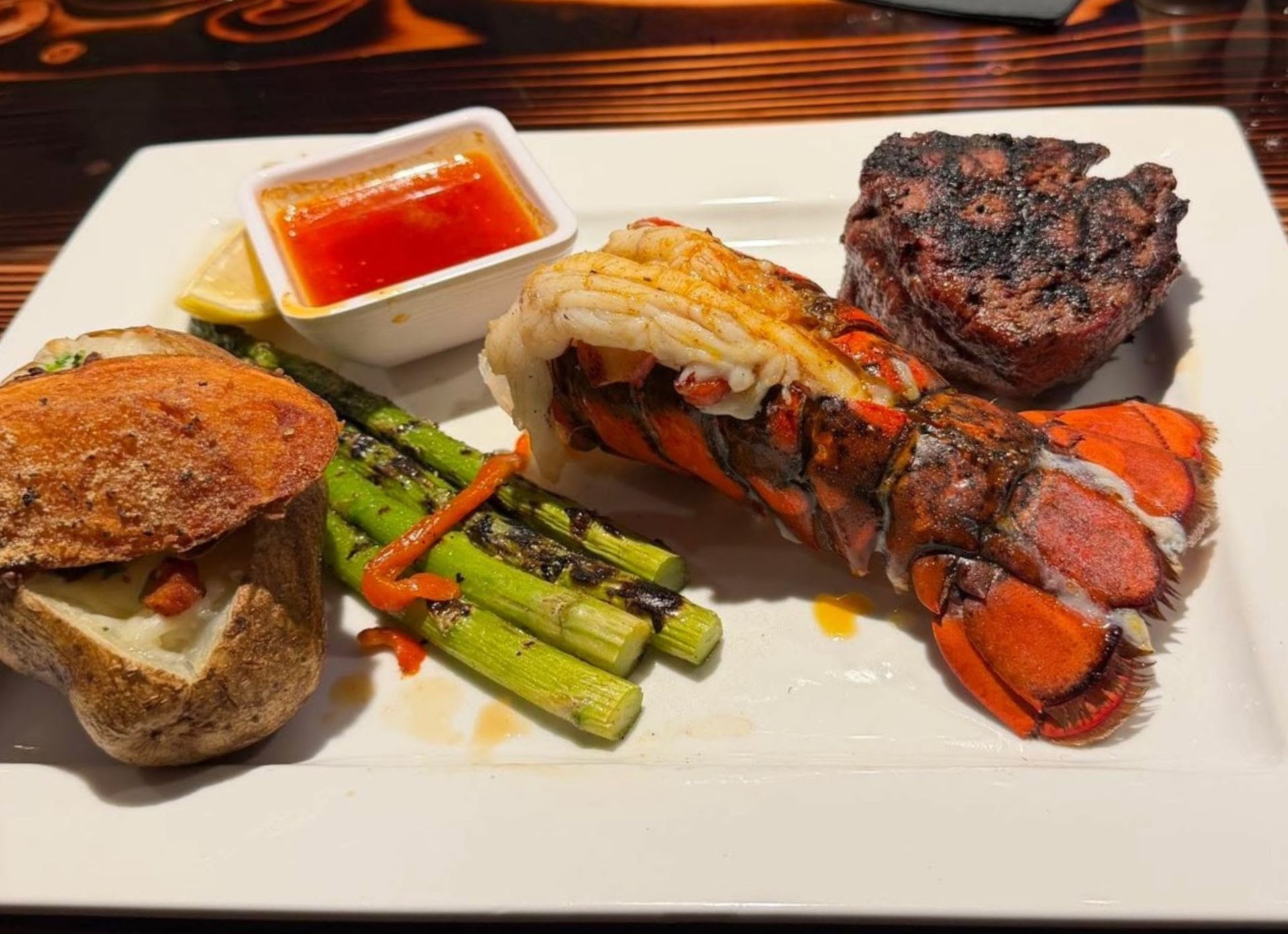 Plated lobster and steak dinner with vegetables and dipping sauce on a white plate