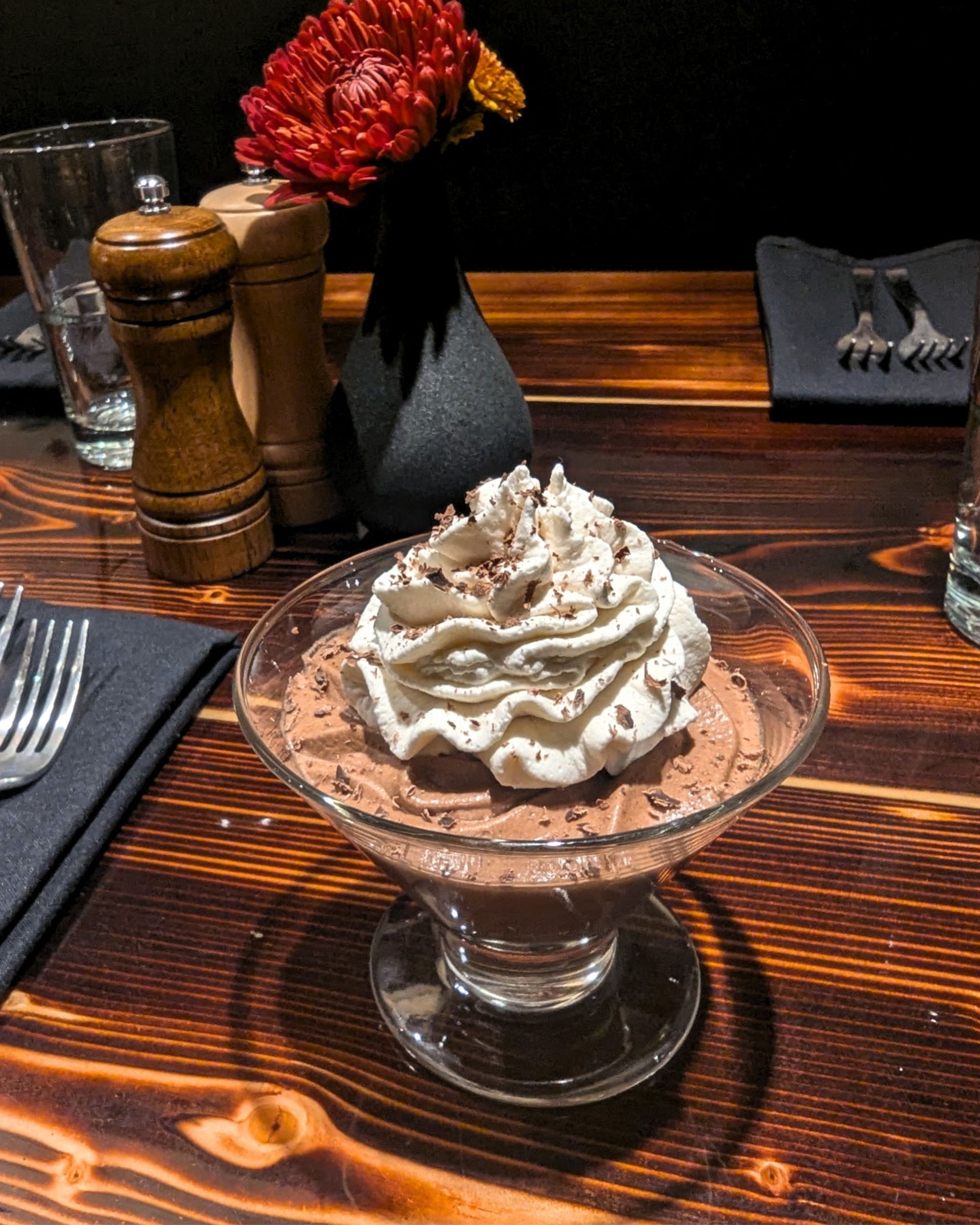 Chocolate dessert topped with whipped cream in a glass dish on a wooden restaurant table