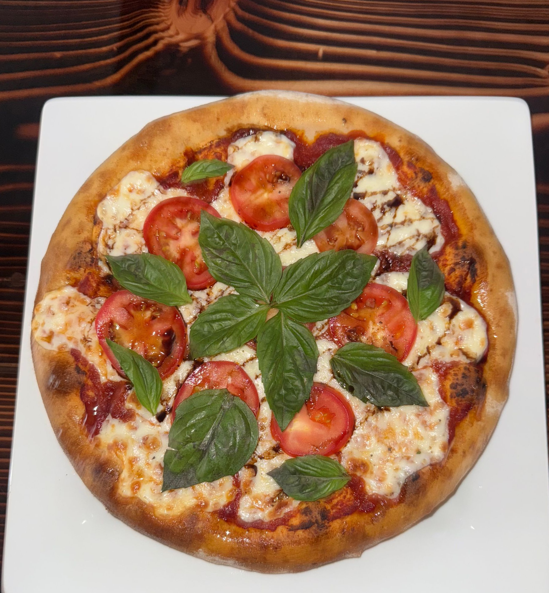 Margherita-style pizza with basil leaves and tomato slices on a white plate
