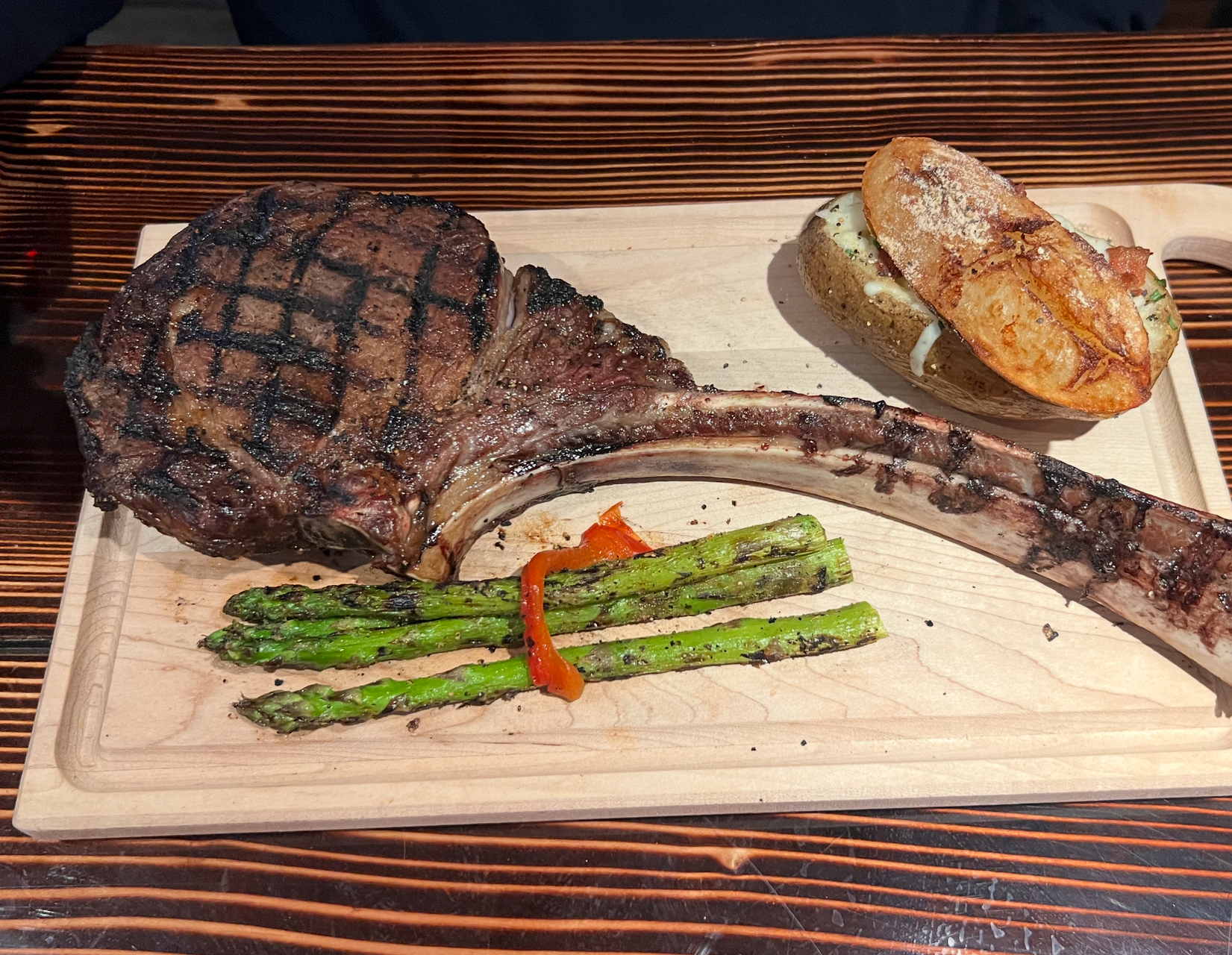 Grilled steak with asparagus and bread on a wooden board, with a grilled rib bone on the side