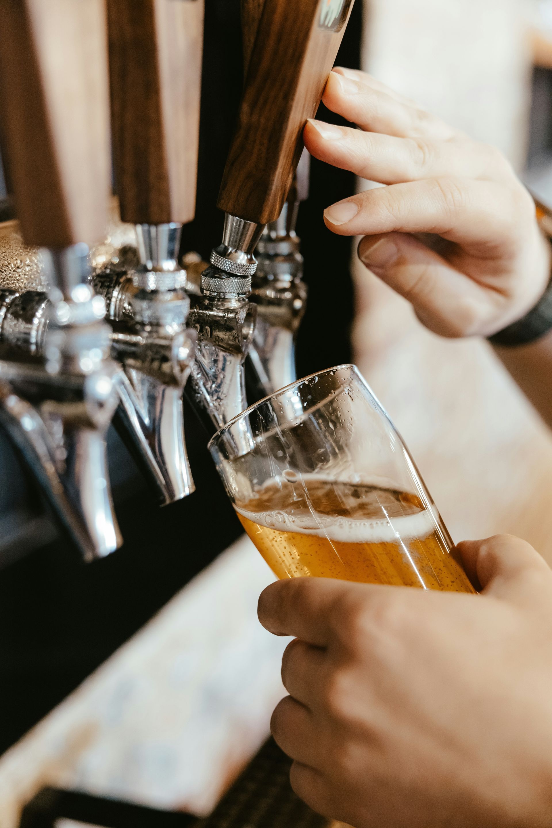 Hands pouring beer from a tap into a tilted glass at a bar