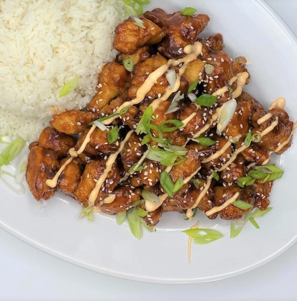 Chicken dish with rice, drizzled sauce, and sesame seeds on a white plate.