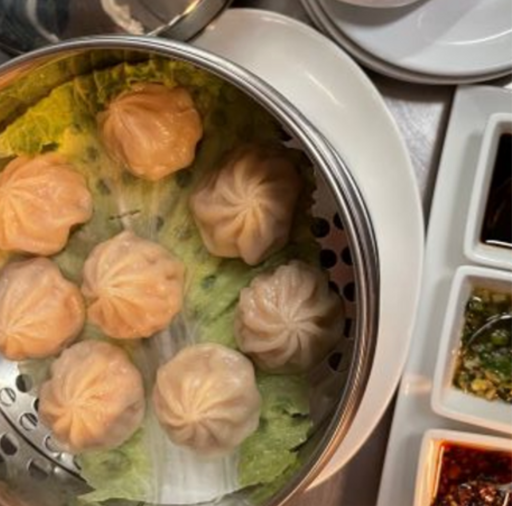 Steamed dumplings in a metal basket with dipping sauces.