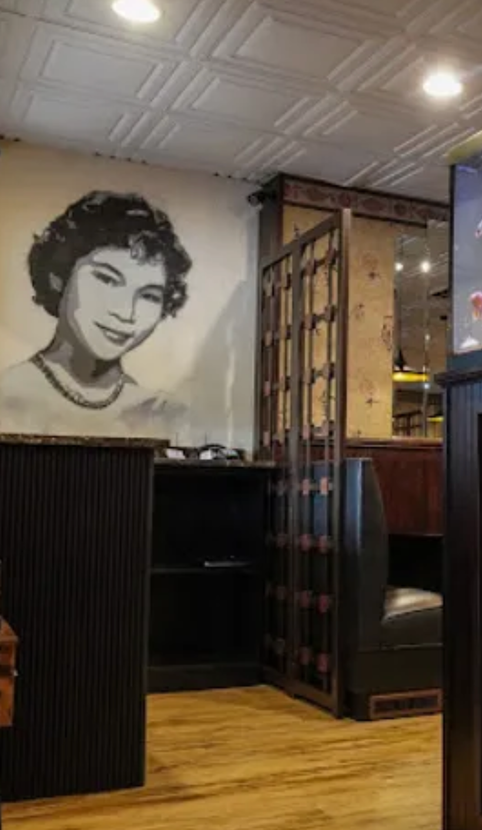 A black and white mural of a smiling woman on a restaurant wall, near a booth and decorative screen.