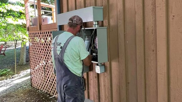 A man is working on an electrical box on the side of a house. A man is working on an electrical box on the side of a house.