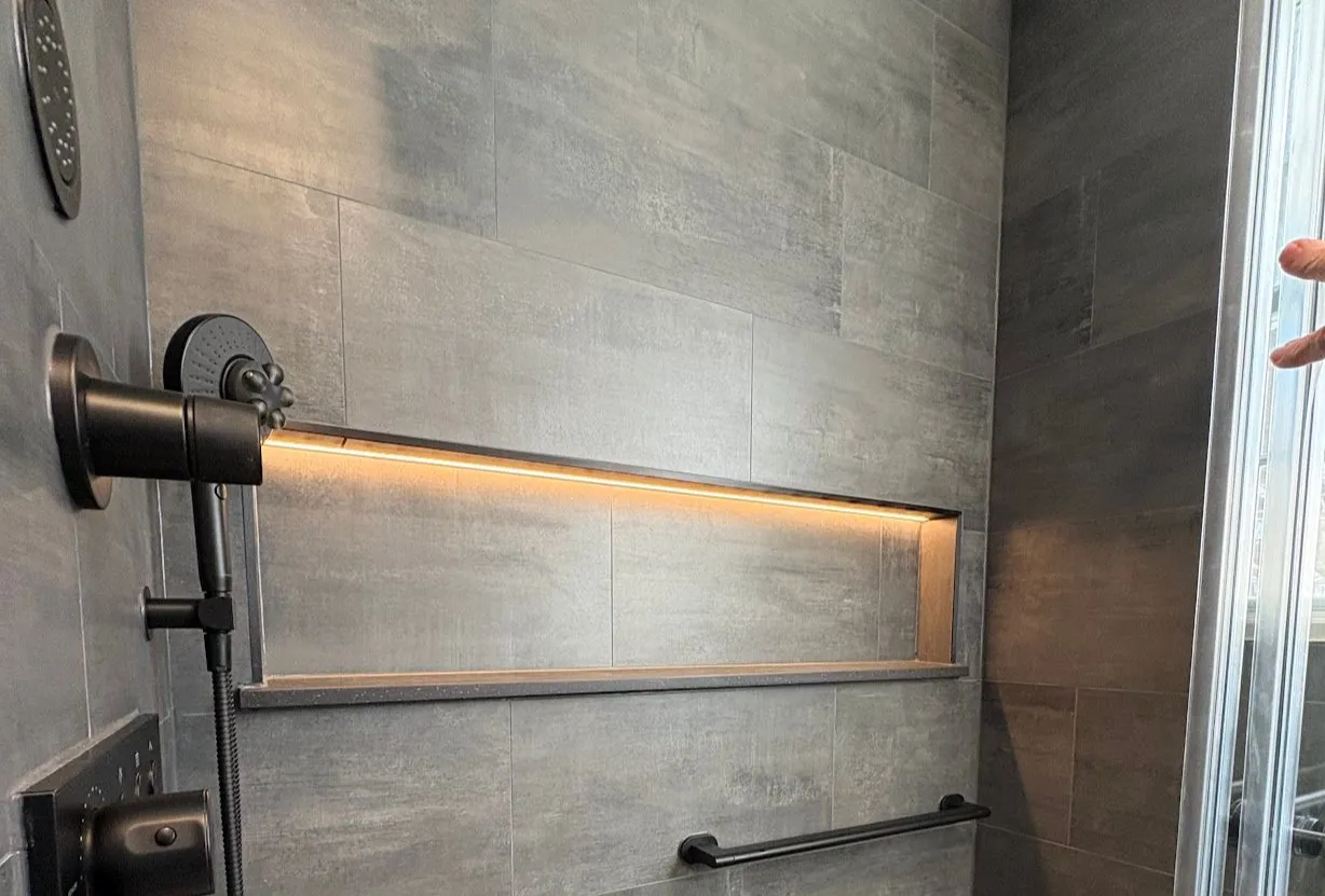 Bathroom with a backlit rectangular mirror above a vanity and a towel bar on a dark tiled wall