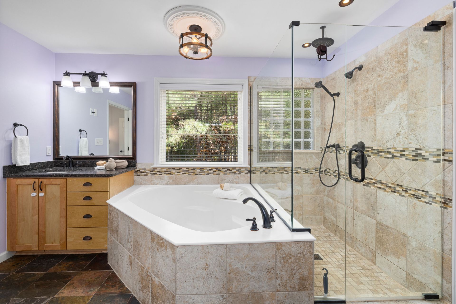 Modern bathroom with double vanity, large mirror, gray tile shower, and hallway view to a bedroom