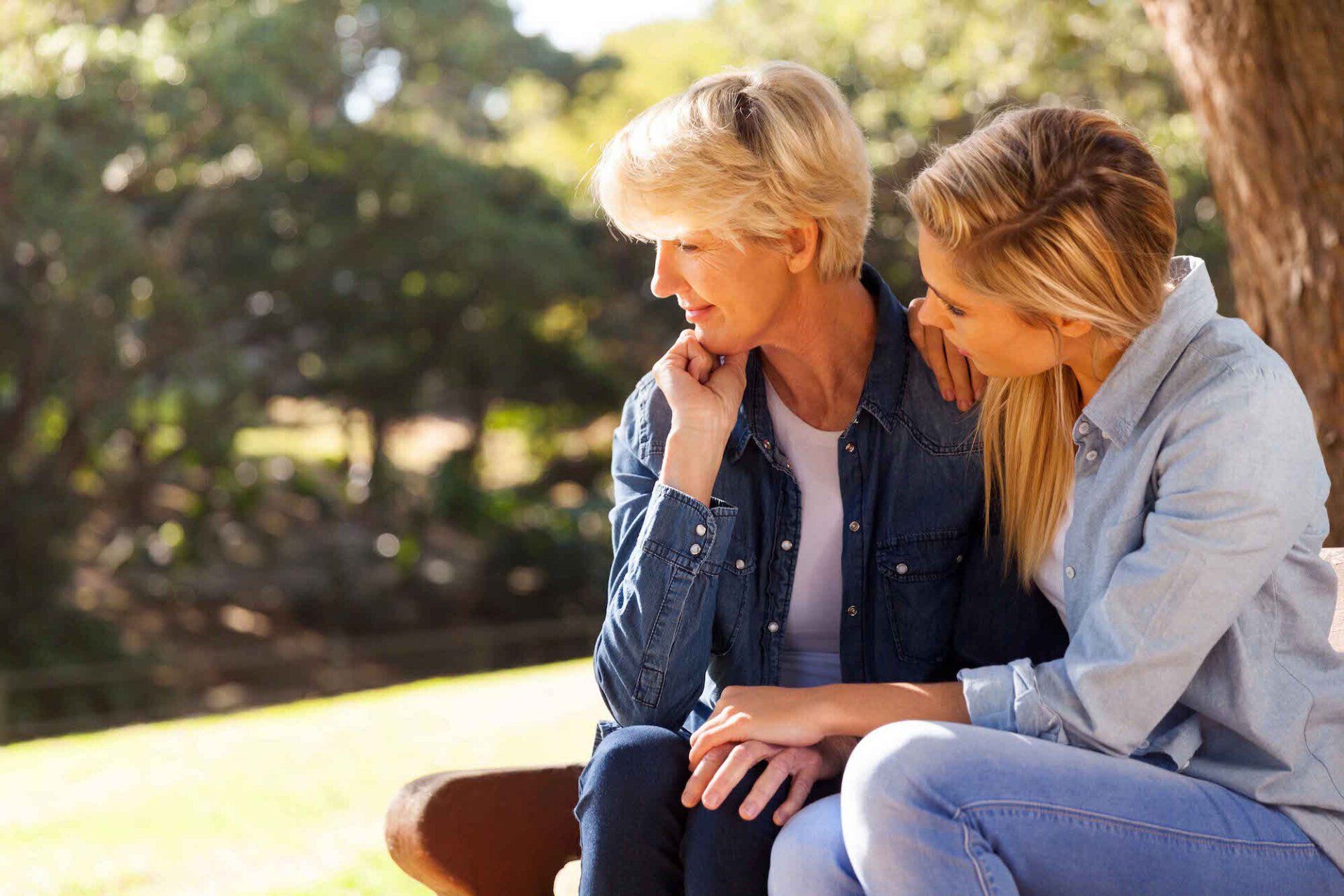 a mother and daughter sit on a bench under a tree