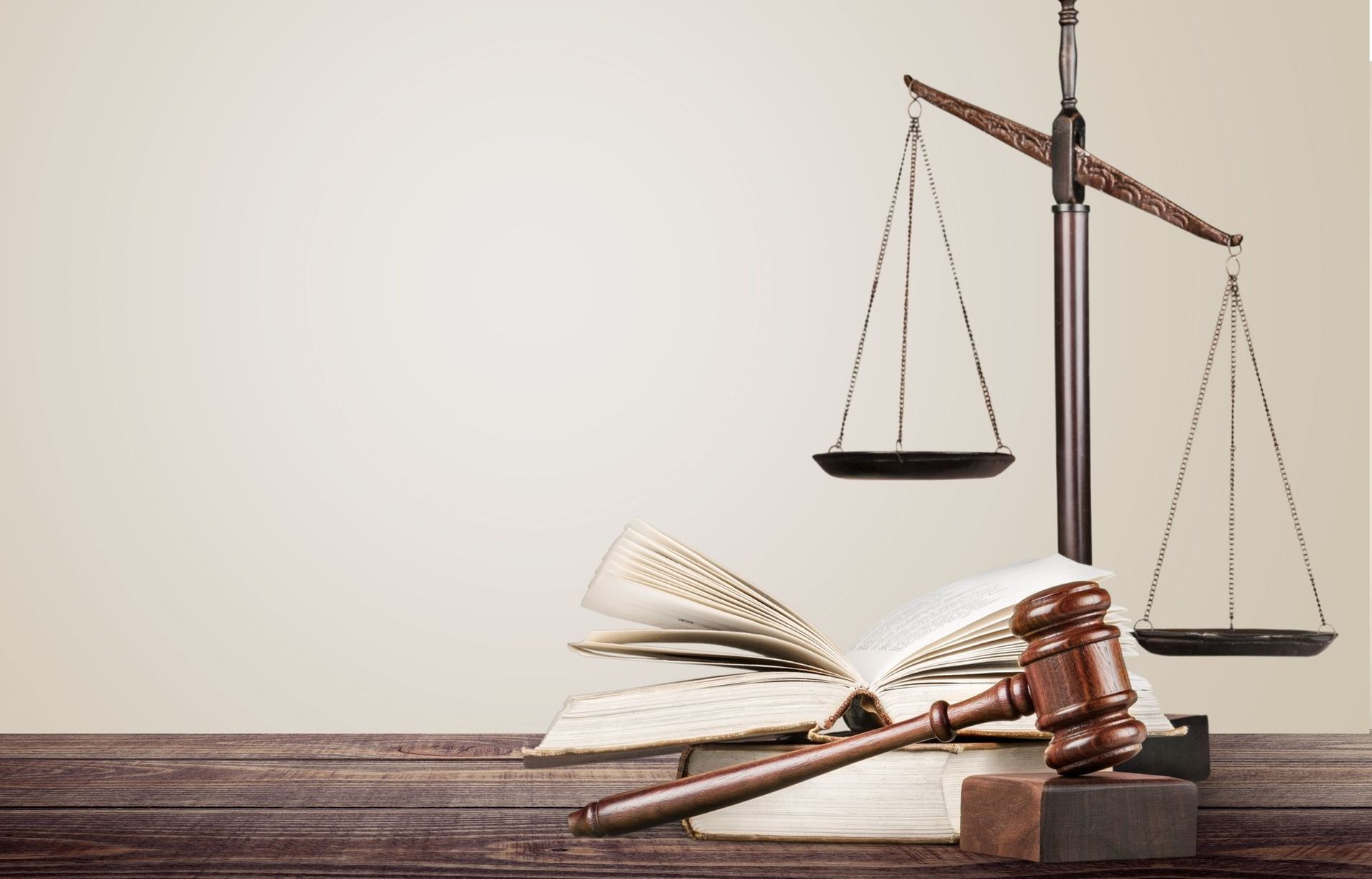Law books and gavel on a wooden desk with balanced scales of justice behind them