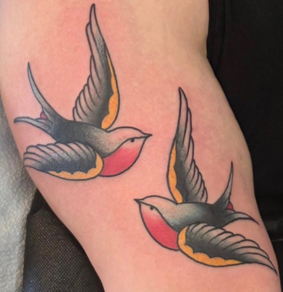 Two colorful swallow tattoos on skin, with gray wings, red bodies, and yellow accents