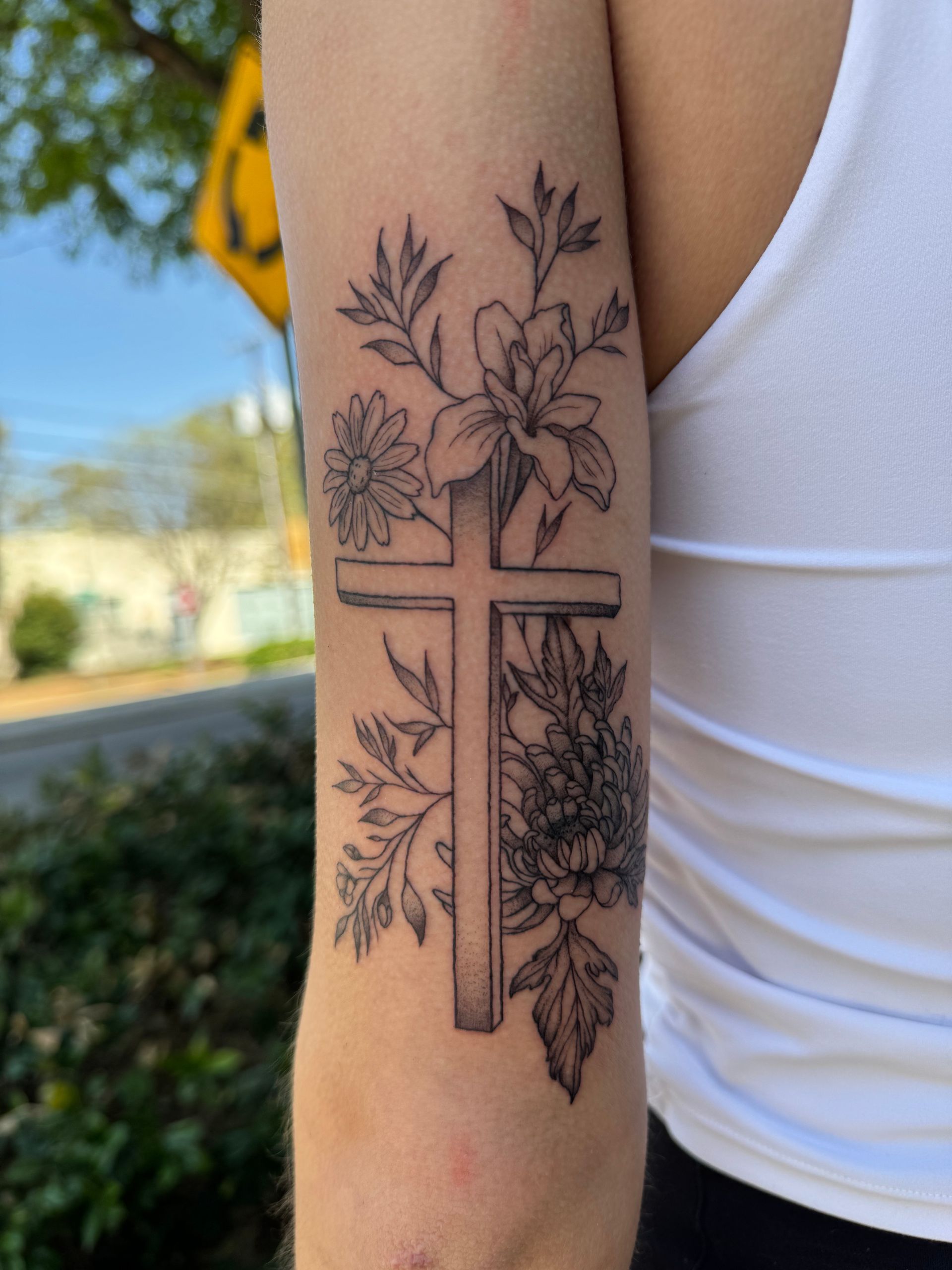 Forearm tattoo of a cross surrounded by floral and leafy designs
