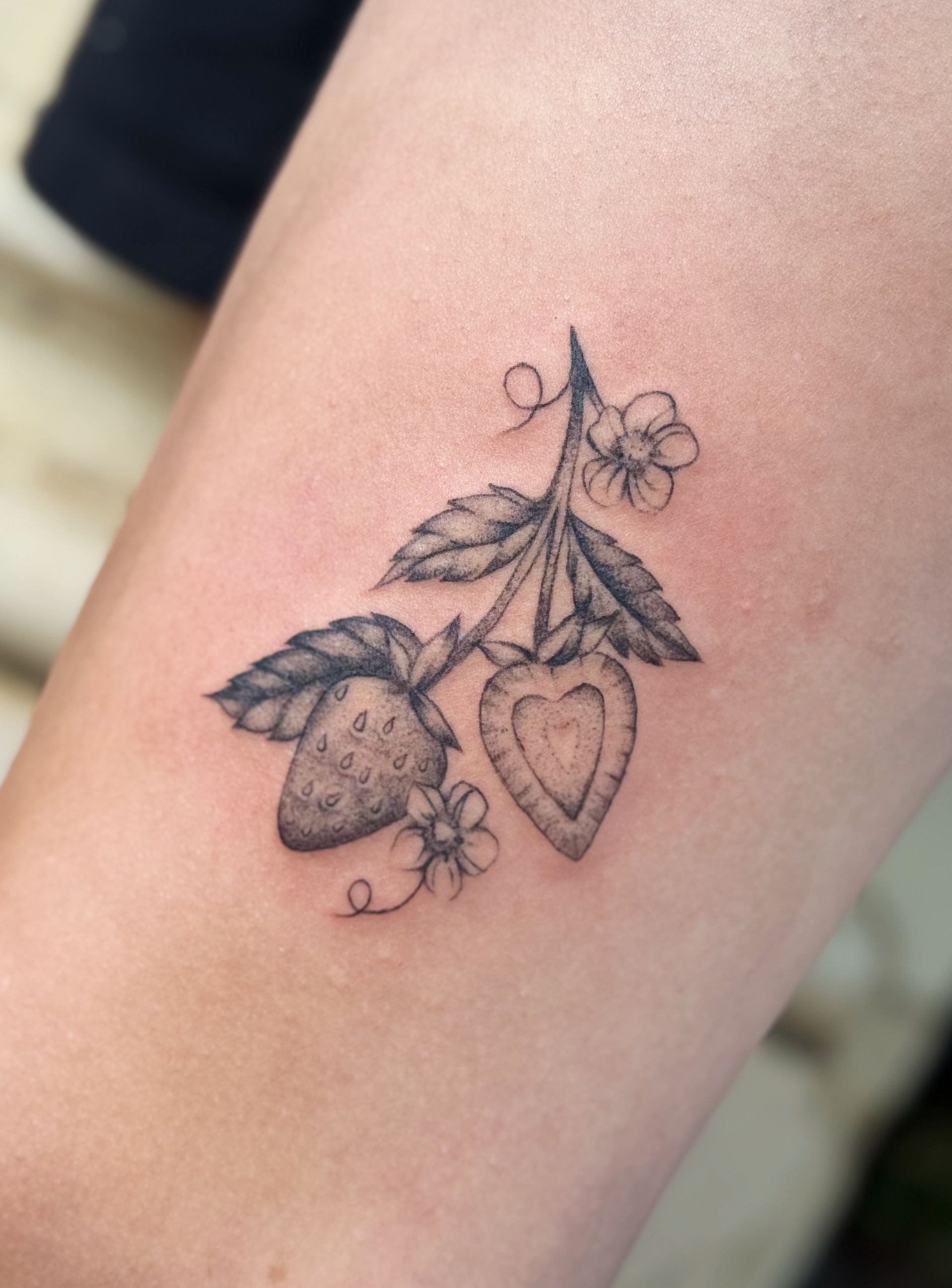 Black-and-gray tattoo of strawberries and leaves on skin