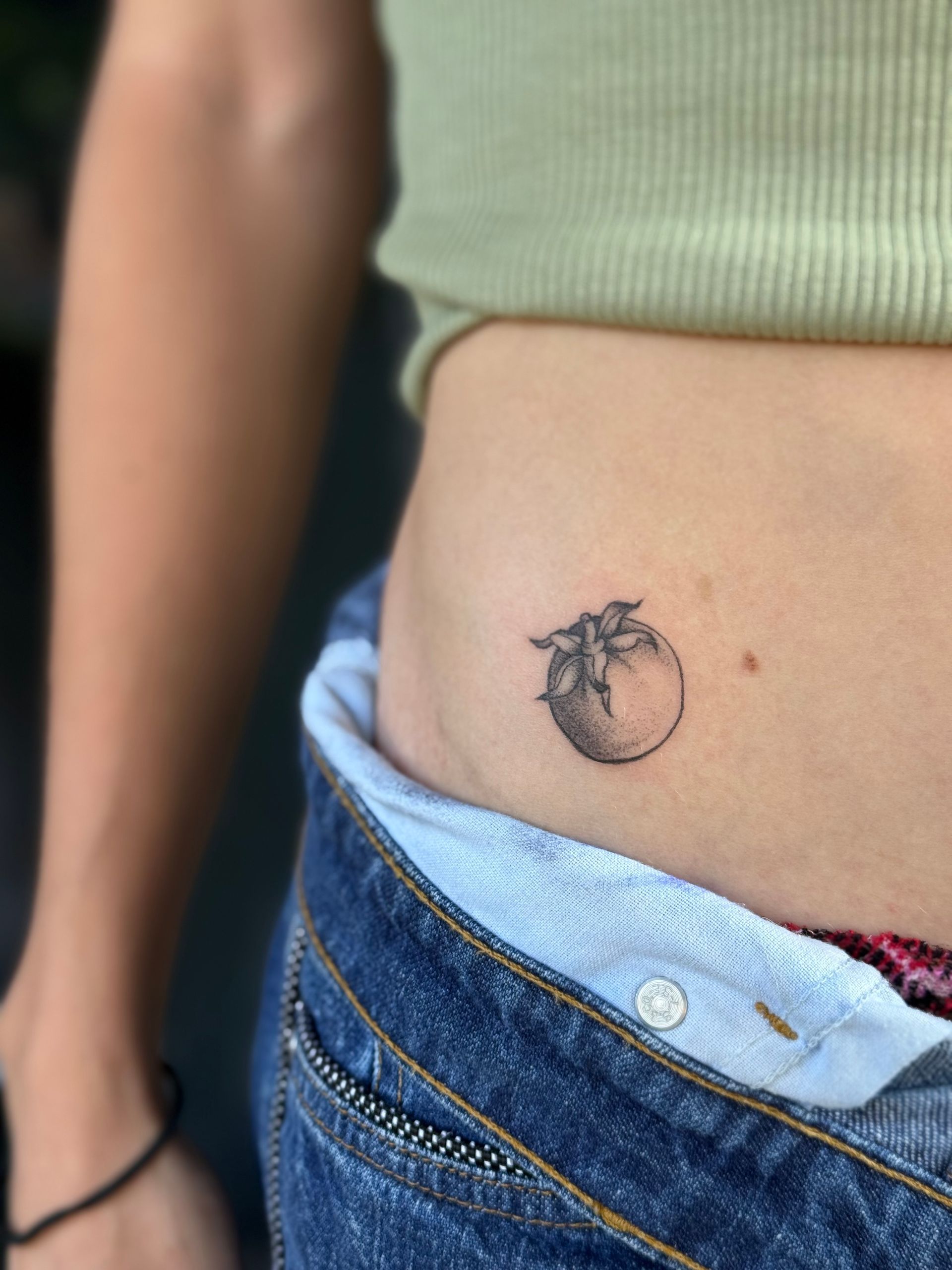 Close-up of a waist with a small dark tattoo near the hip above blue jeans