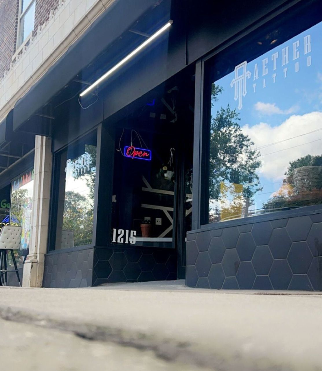 Storefront with dark facade, reflective windows, and a neon open sign by the entrance