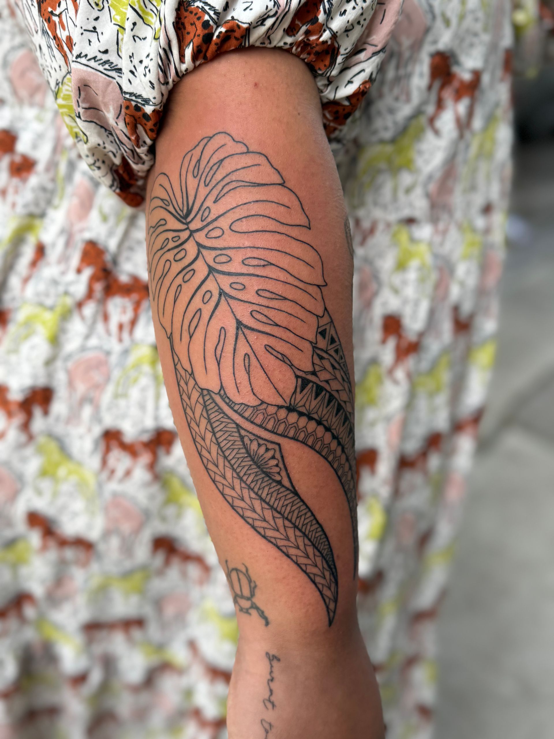 Arm with large floral tattoo in black ink against a colorful patterned fabric background