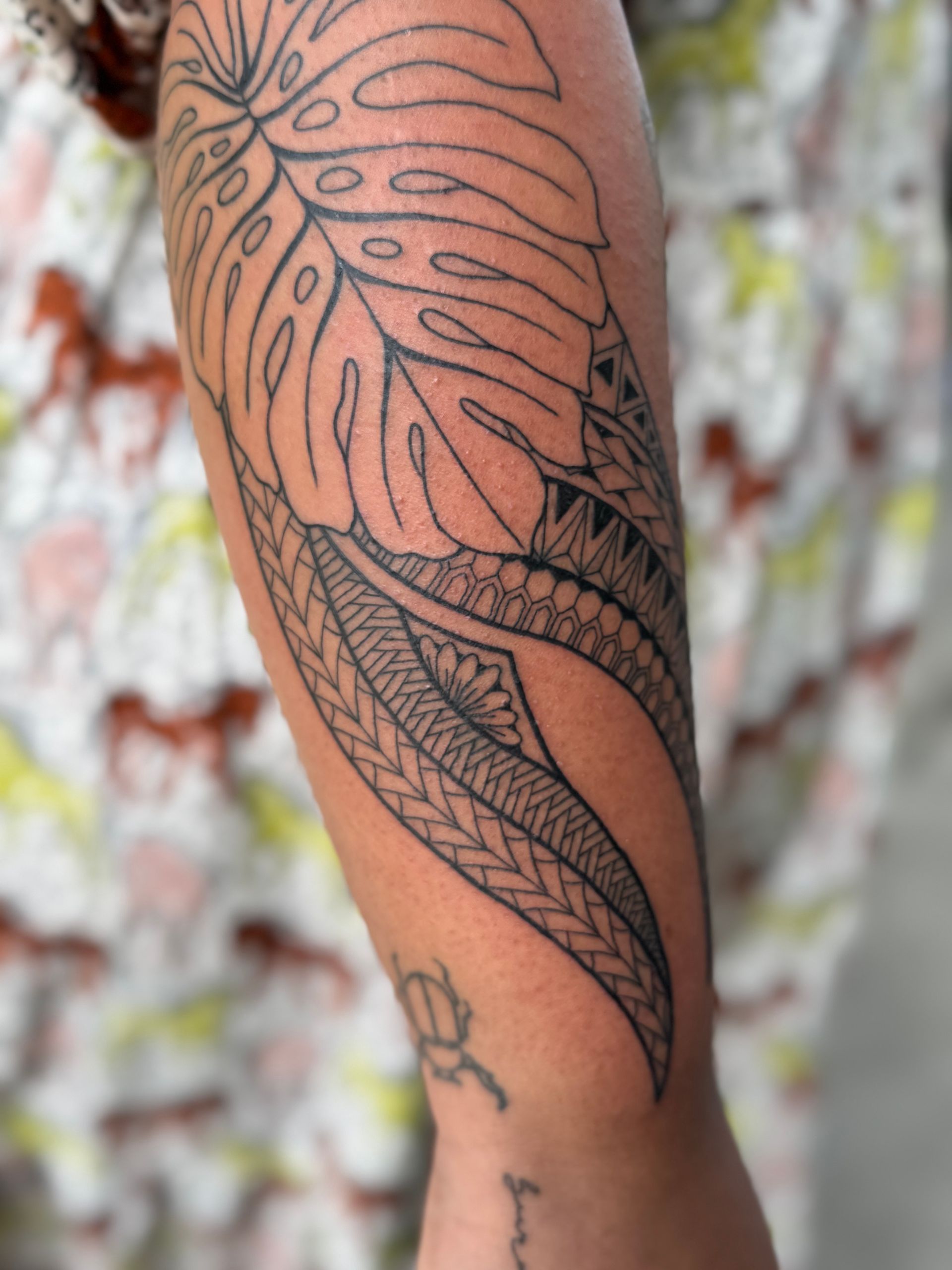 Close-up of a forearm with a large black leaf tattoo on tan skin.