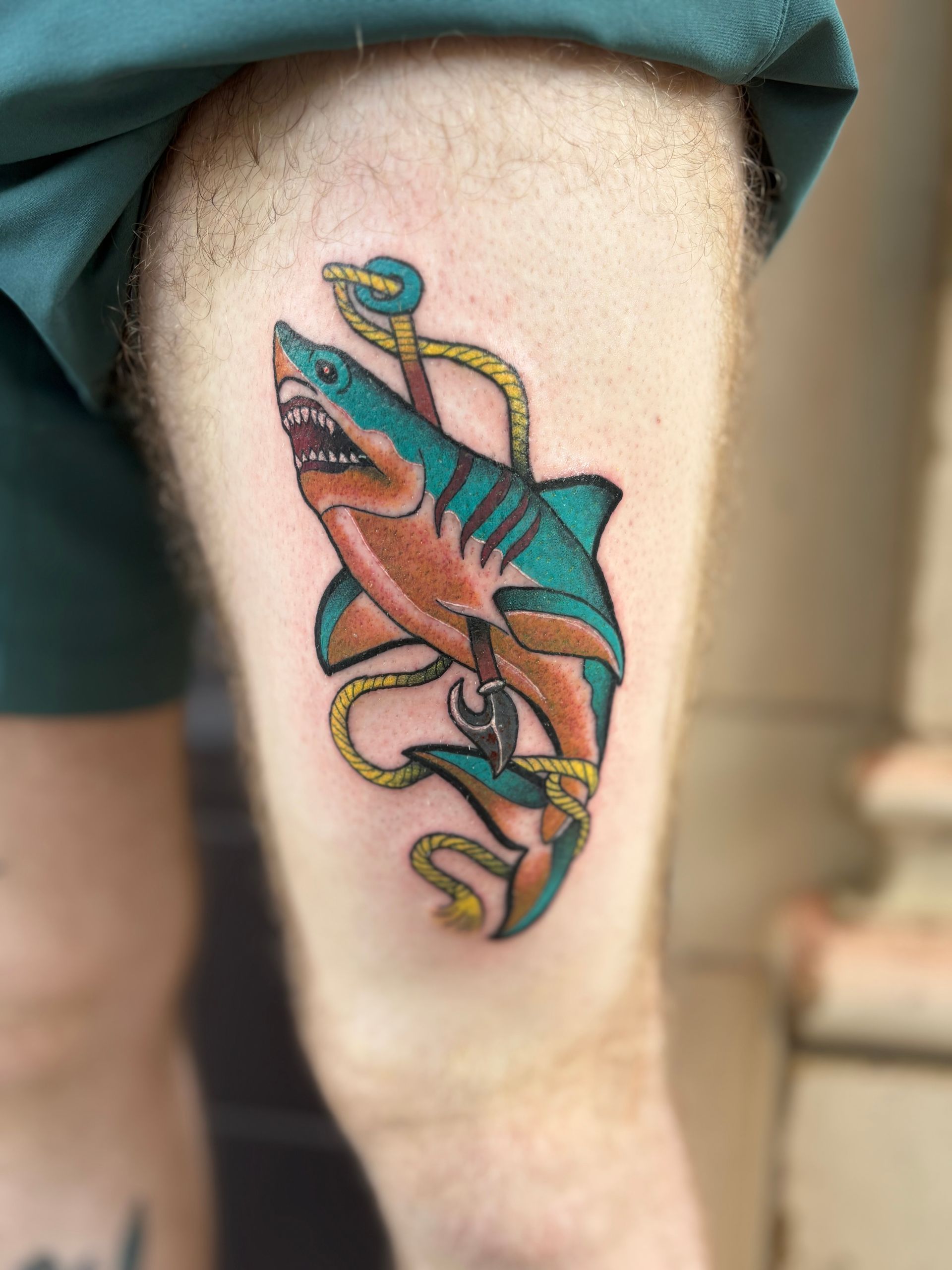 Colorful fish tattoo on a person’s calf, with blue and pink shading and looping rope-like details