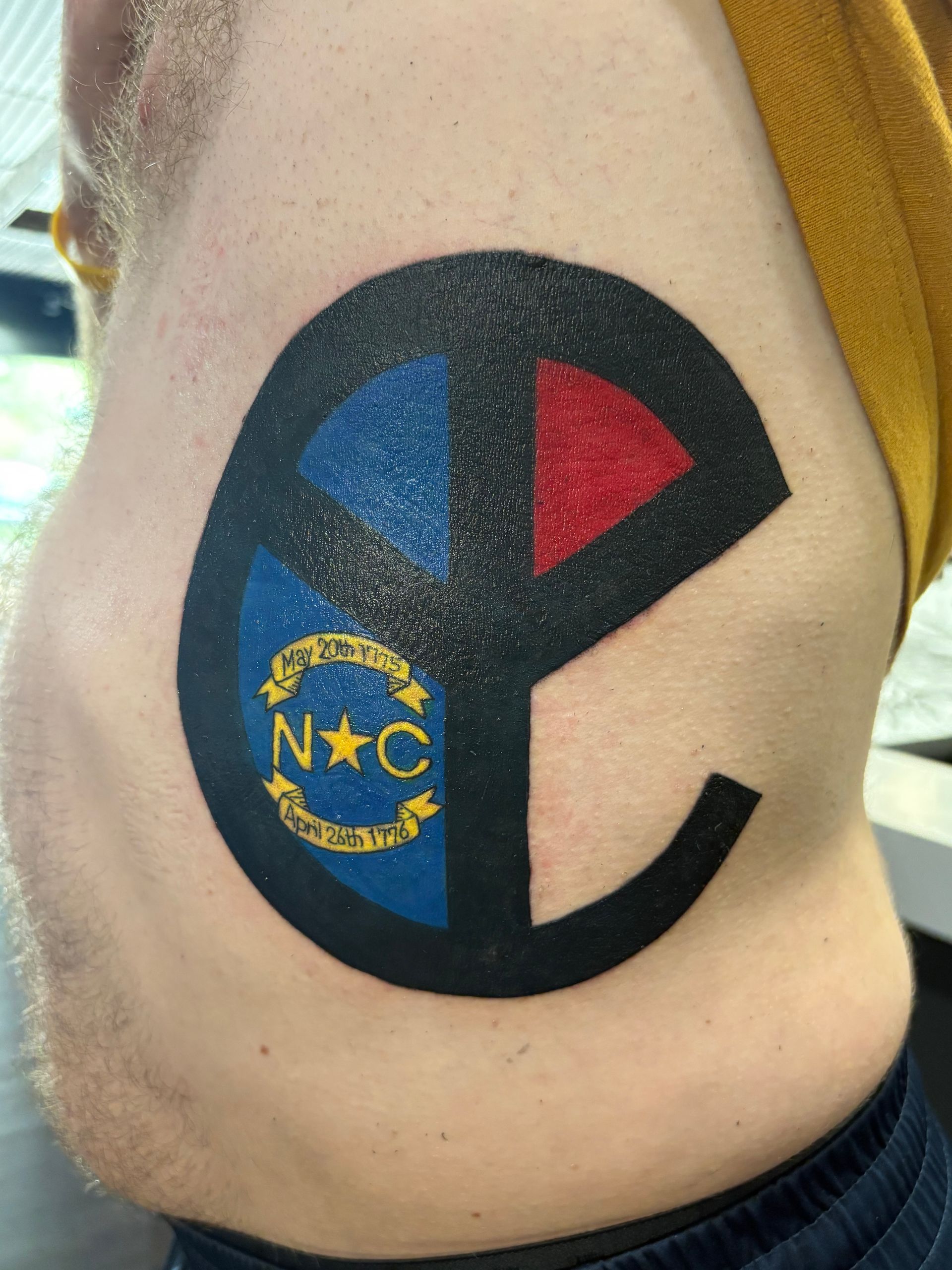 Black-and-blue sports tattoo with red and blue triangles and yellow “NC” on a person’s side