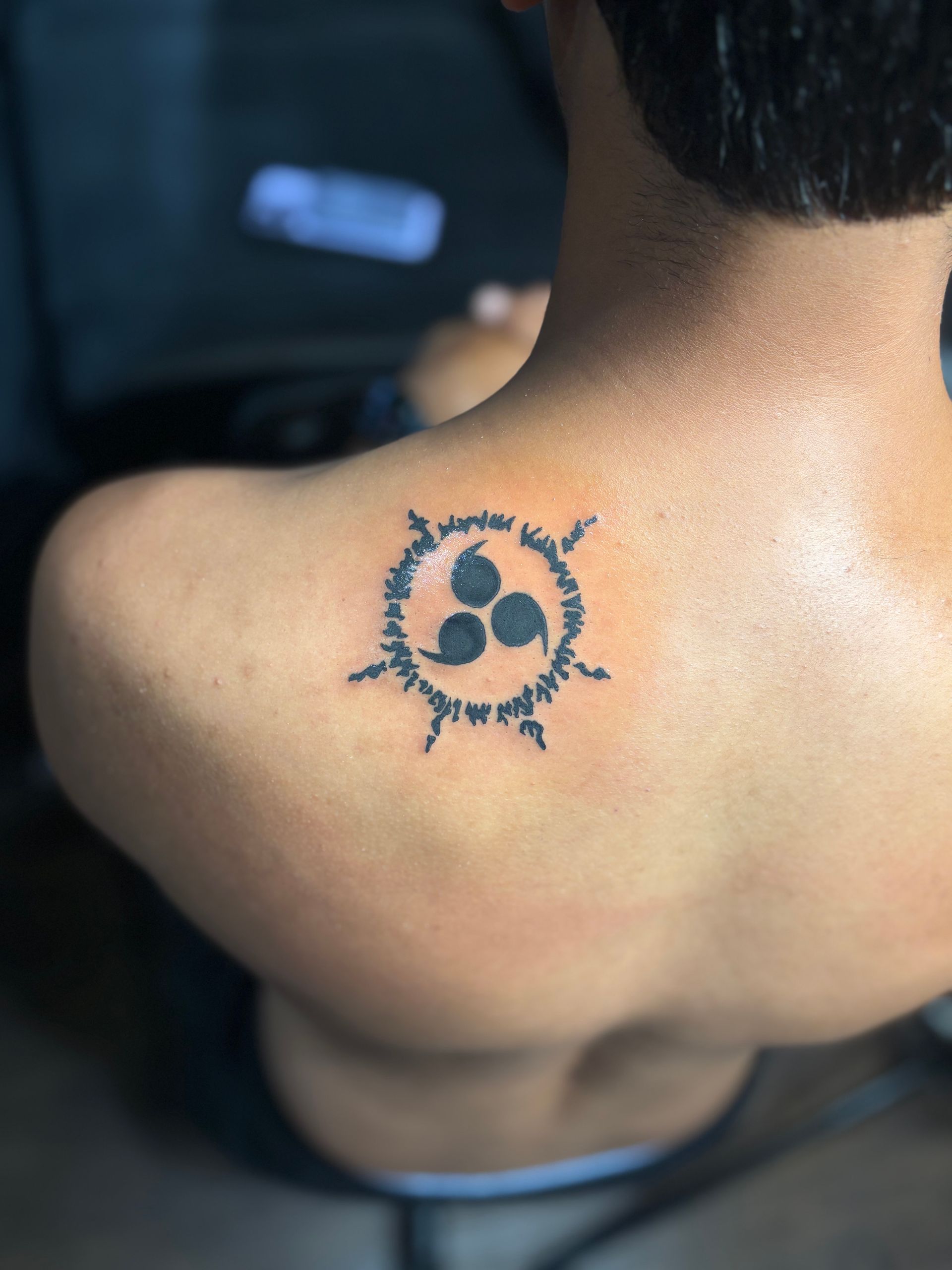 Close-up of a shoulder with a small black sun tattoo, outdoors in bright light