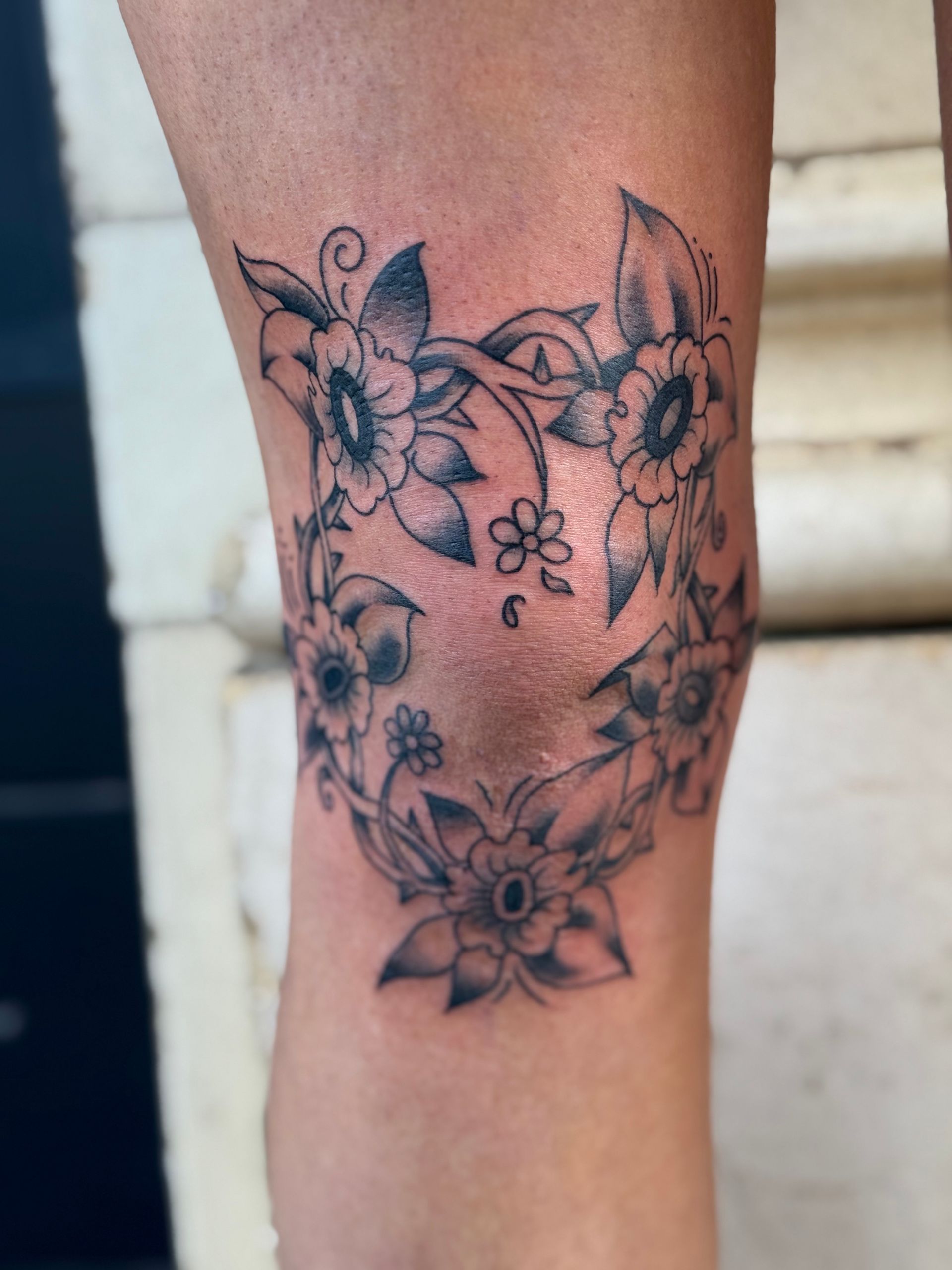 Black floral tattoo on a person’s forearm with flowers and leafy swirls