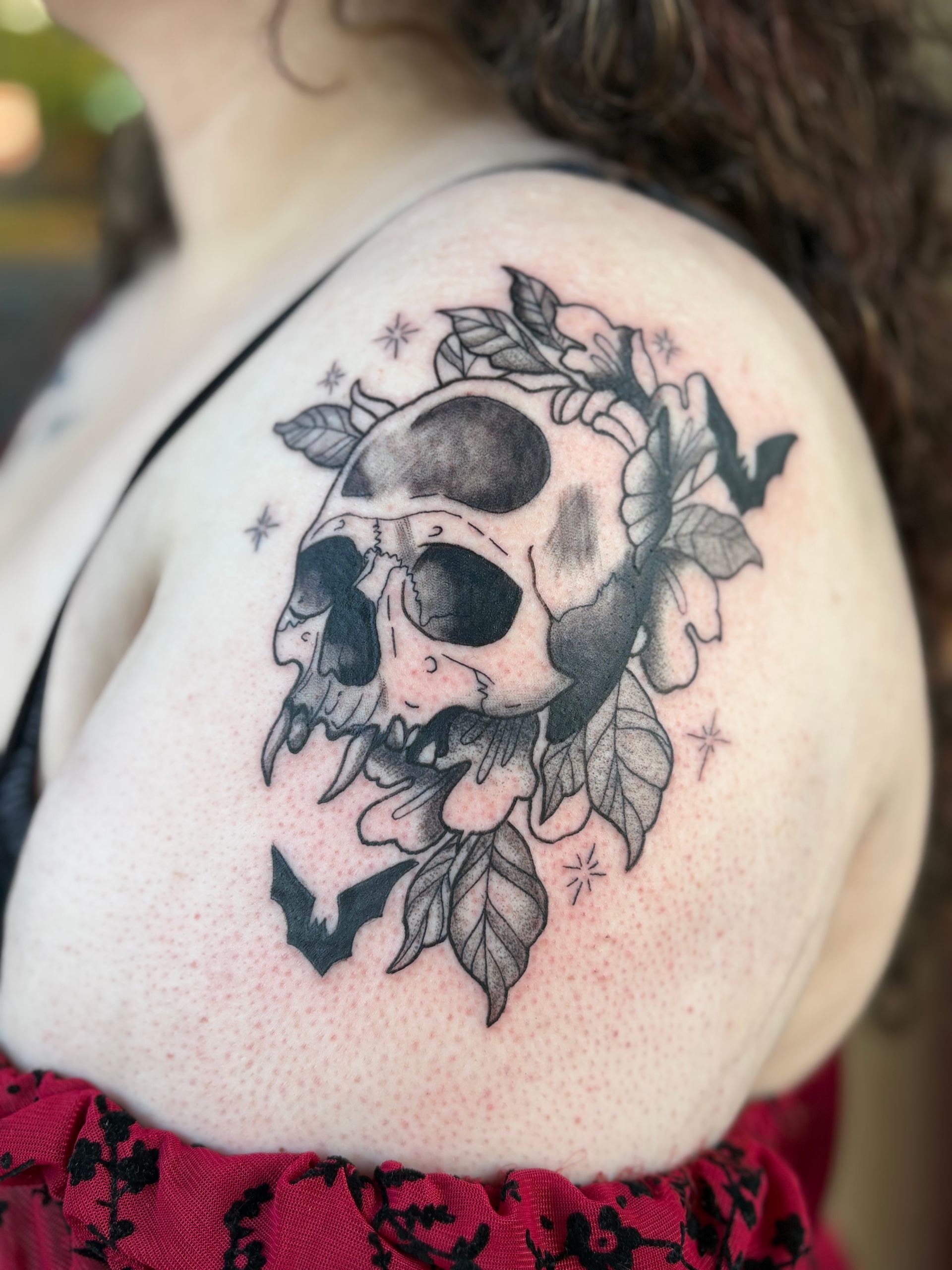 Black skull and floral tattoo on a person’s shoulder with small star accents