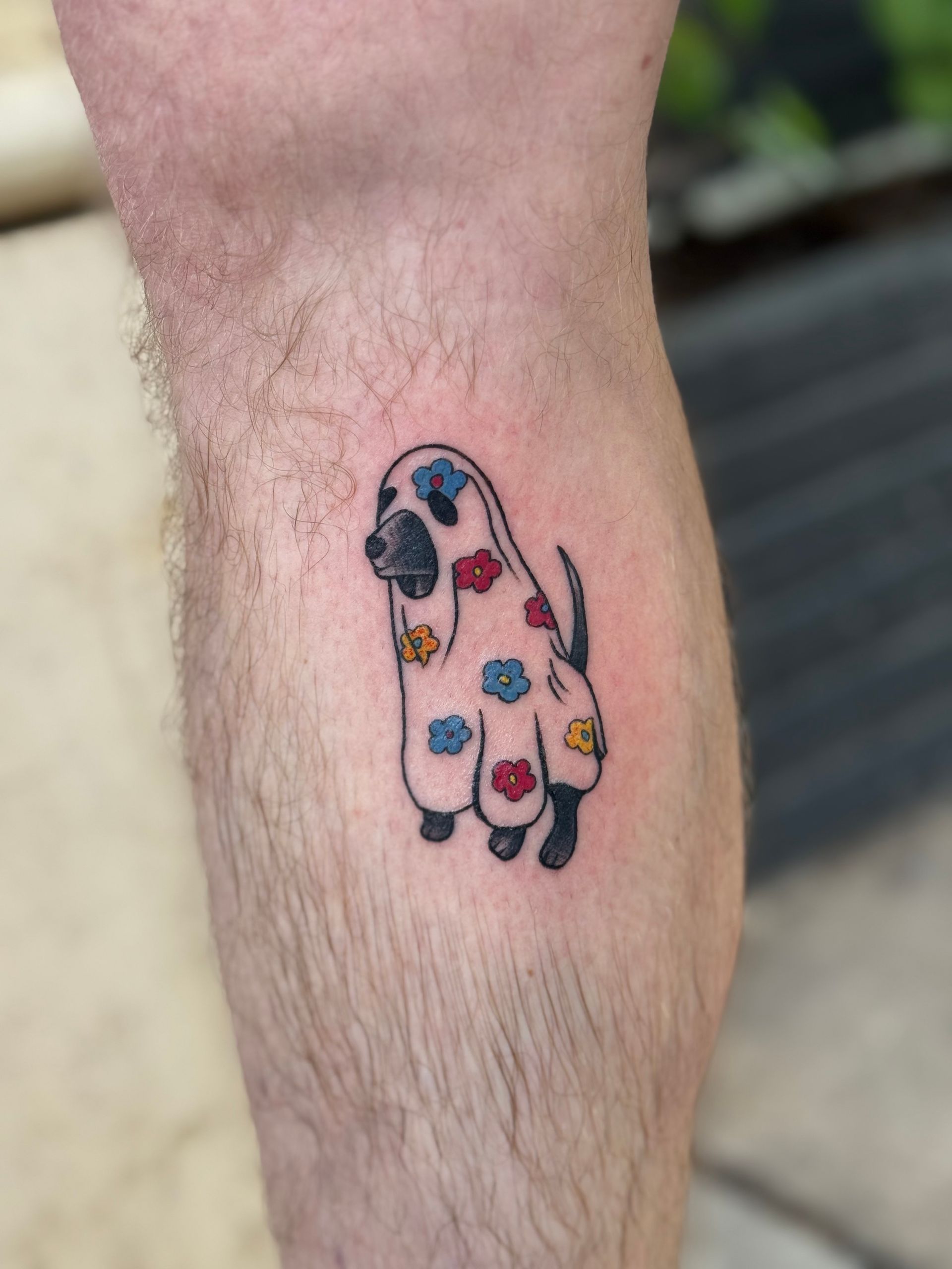 Close-up of a colorful paw-print tattoo on a hairy ankle.
