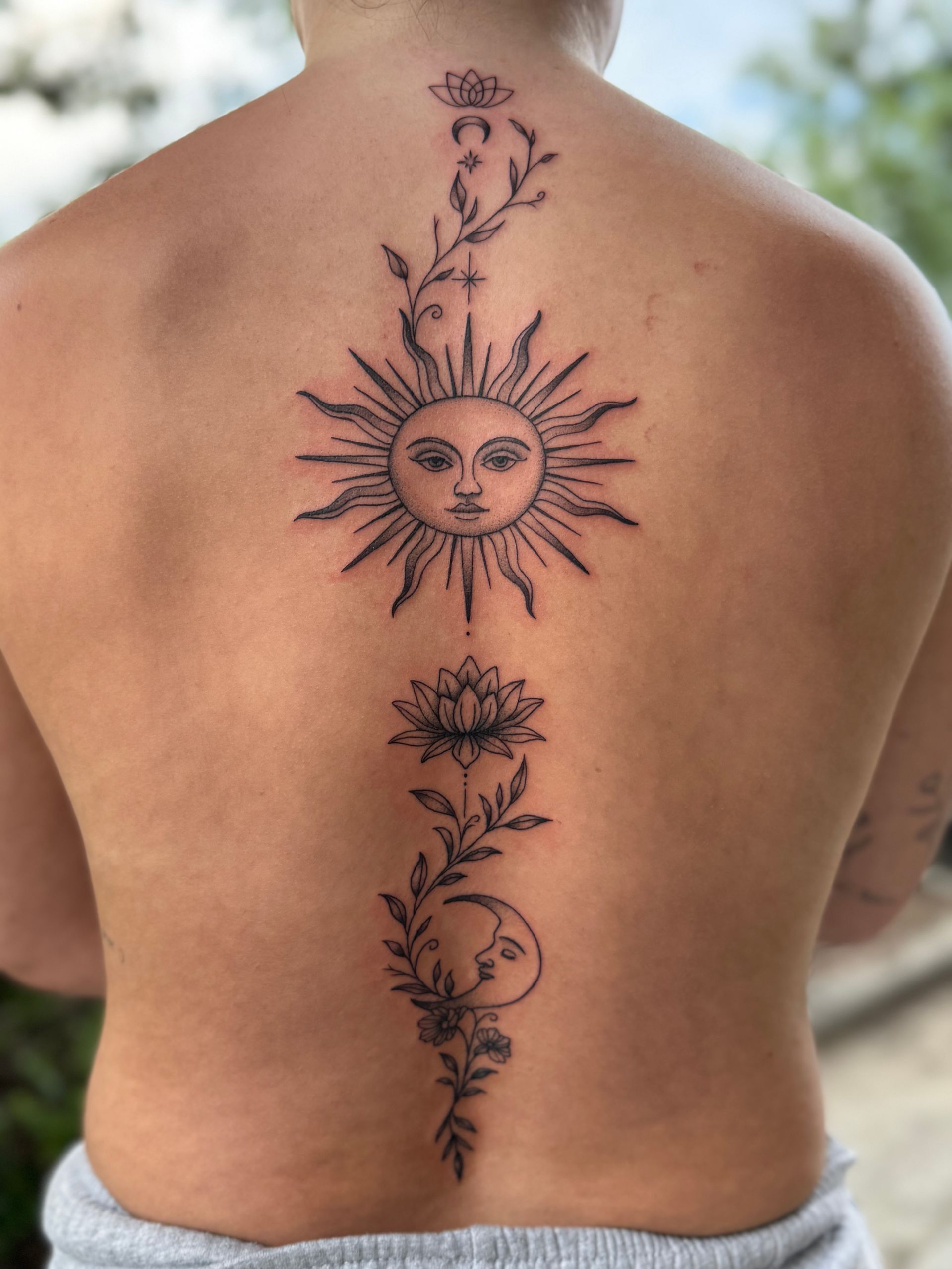 Back tattoo of a sun and floral vine design on a bare back