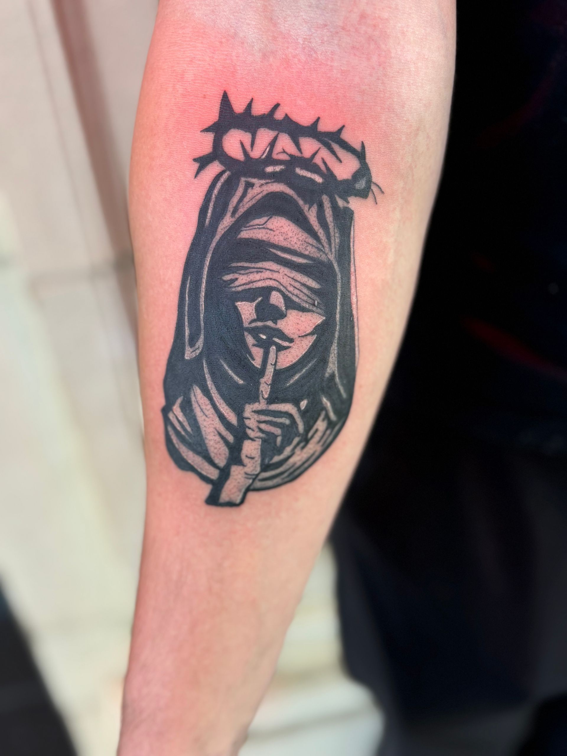 Black tattoo of a crowned hooded face on a person’s calf, with red irritated skin around it