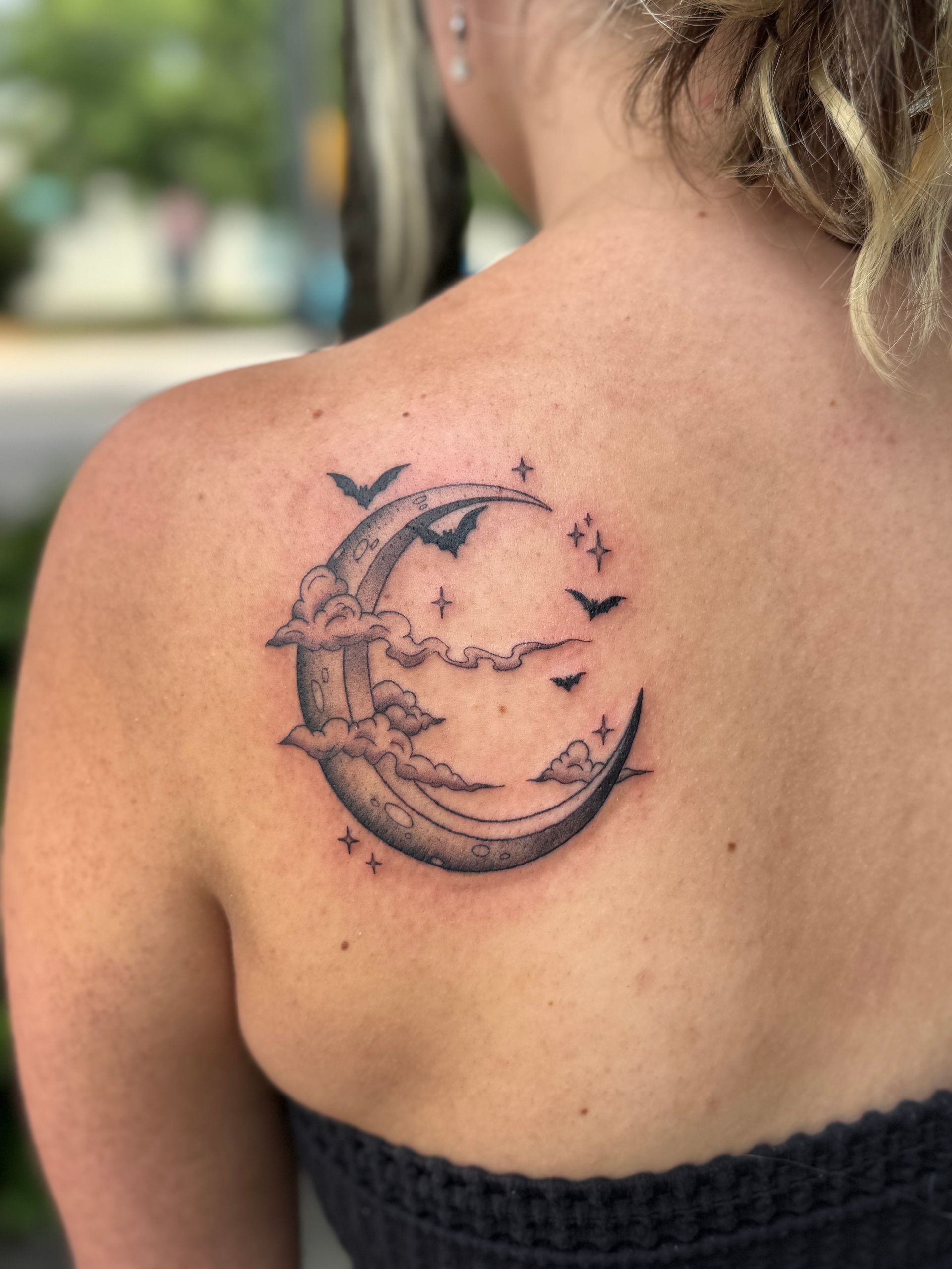 Moon and stars tattoo on a person's upper back and shoulder, with a crescent moon and small birds.