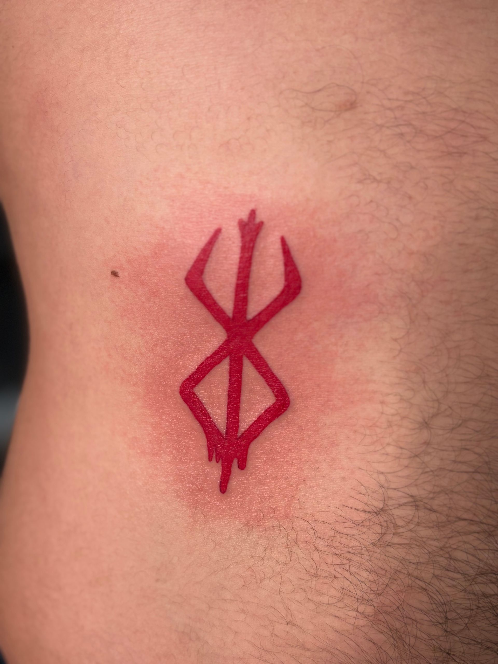 Red geometric tattoo on skin, with sharp angular lines in dark red ink.