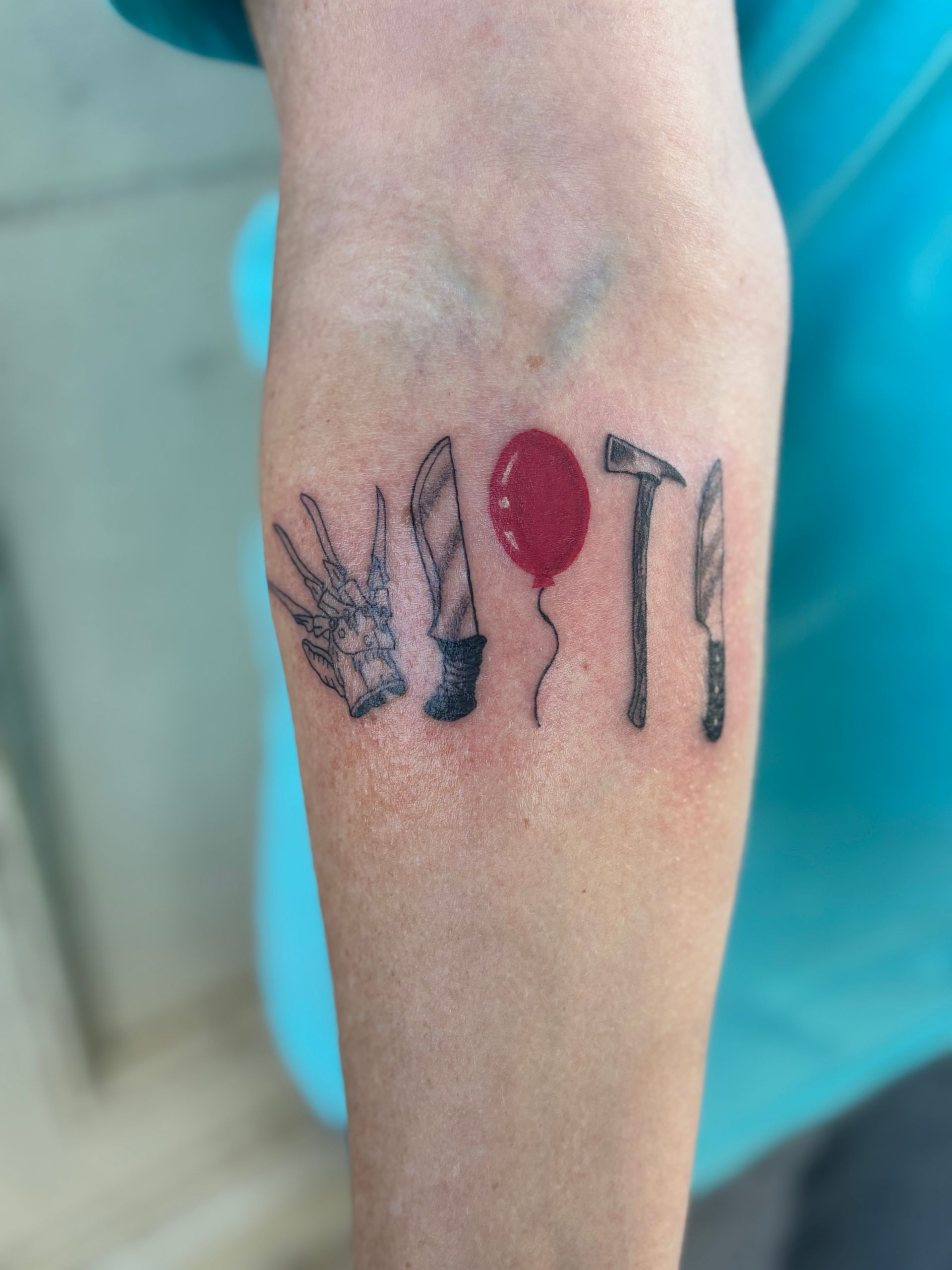 Forearm tattoo with a red balloon and black bird-like shapes on skin
