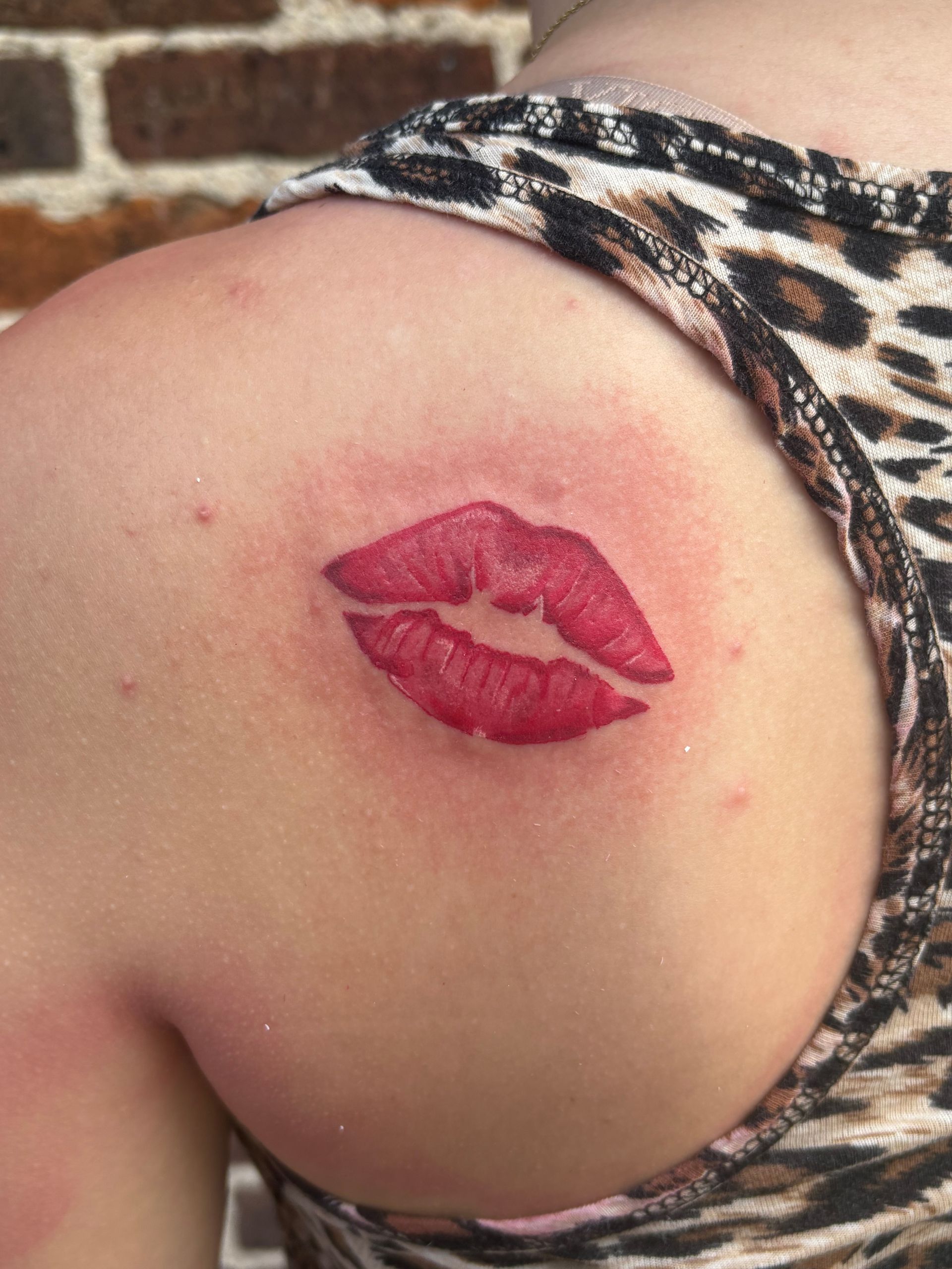 Close-up of a shoulder with a red lipstick kiss mark tattoo or stamp against a brick wall background