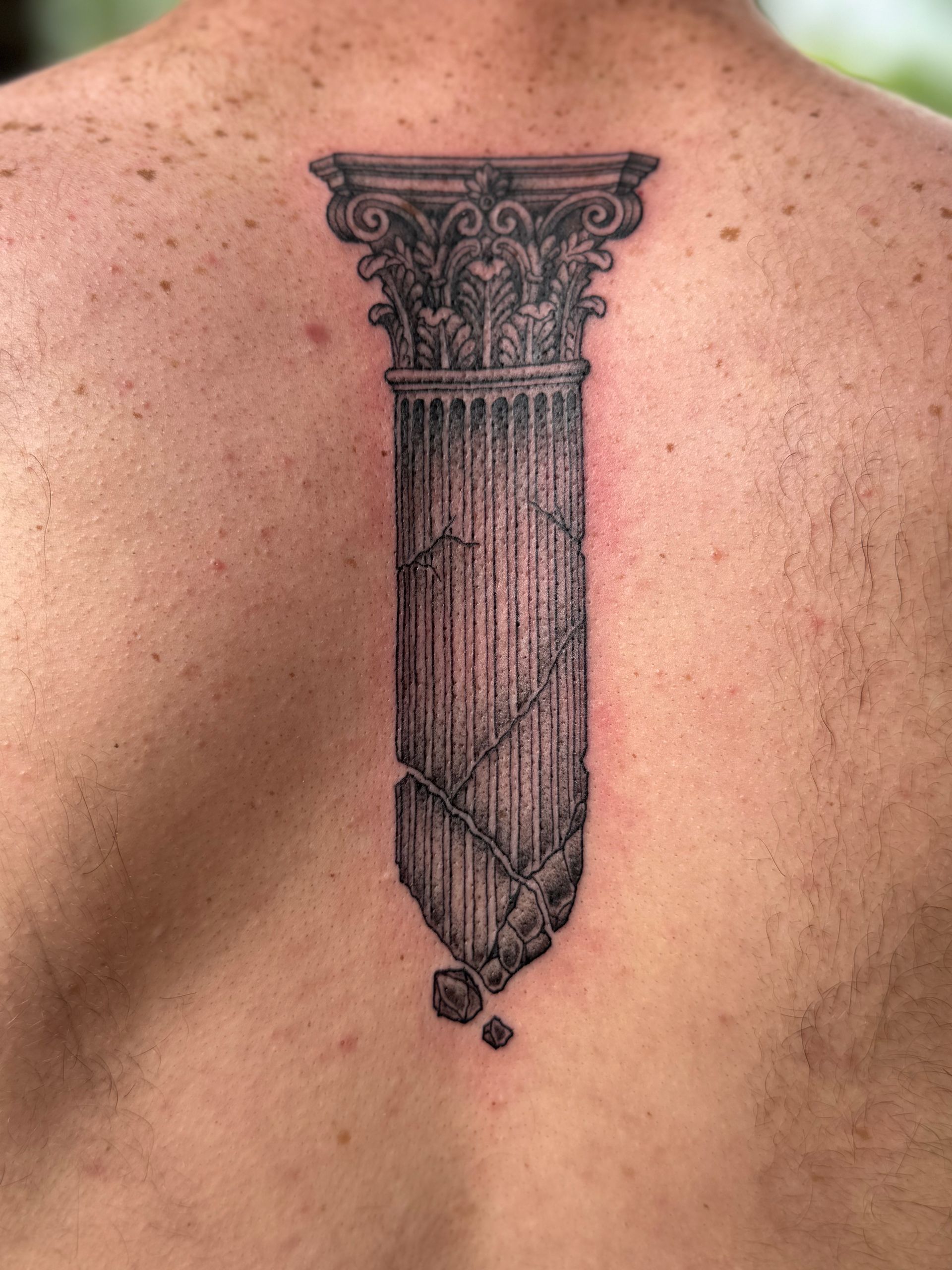 Black tattoo of a classical column on skin, with a cracked, pointed base and decorative capital.