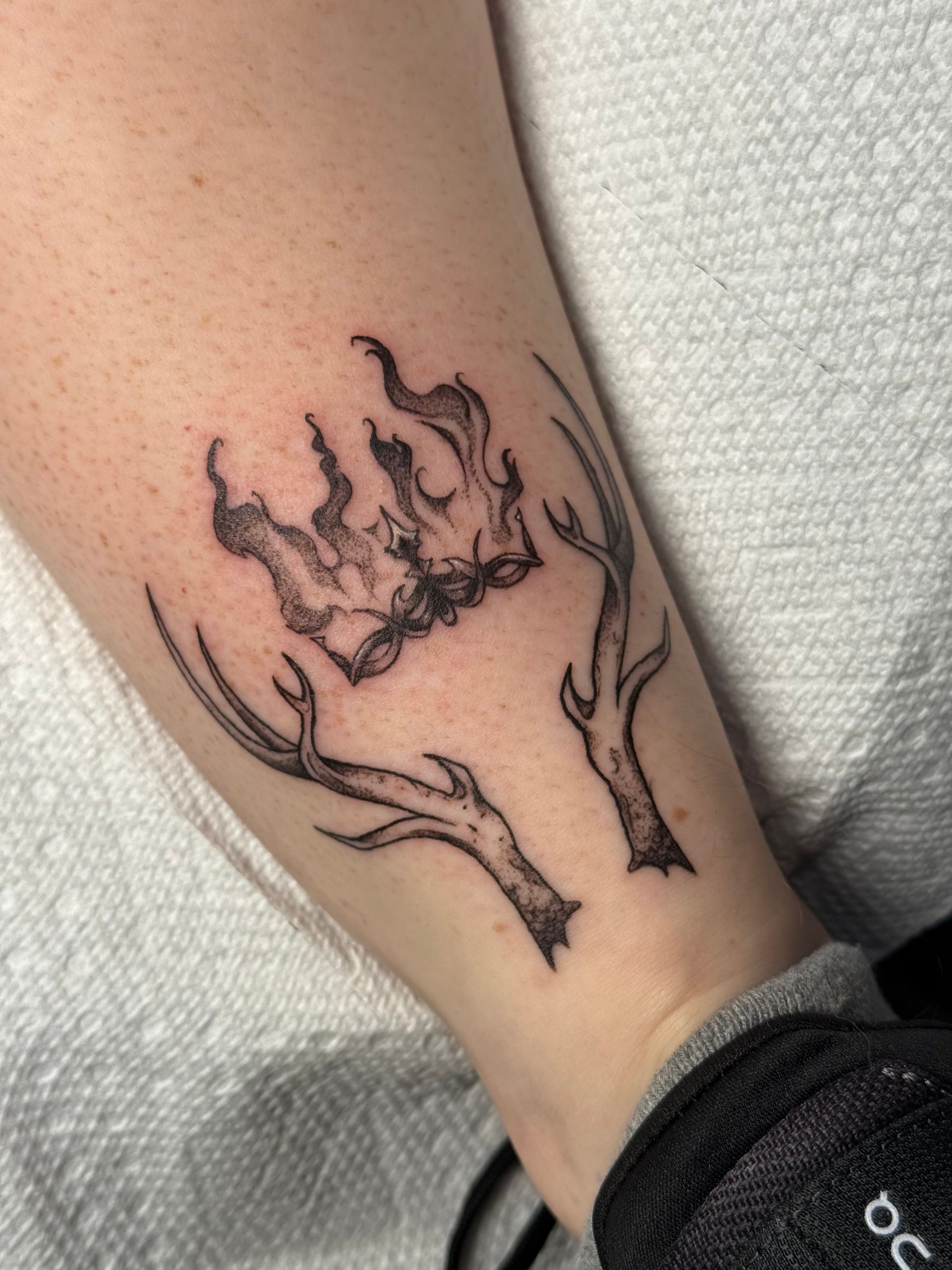 Black line-art tattoo of a crown with antler-like branches on a forearm, on a white background