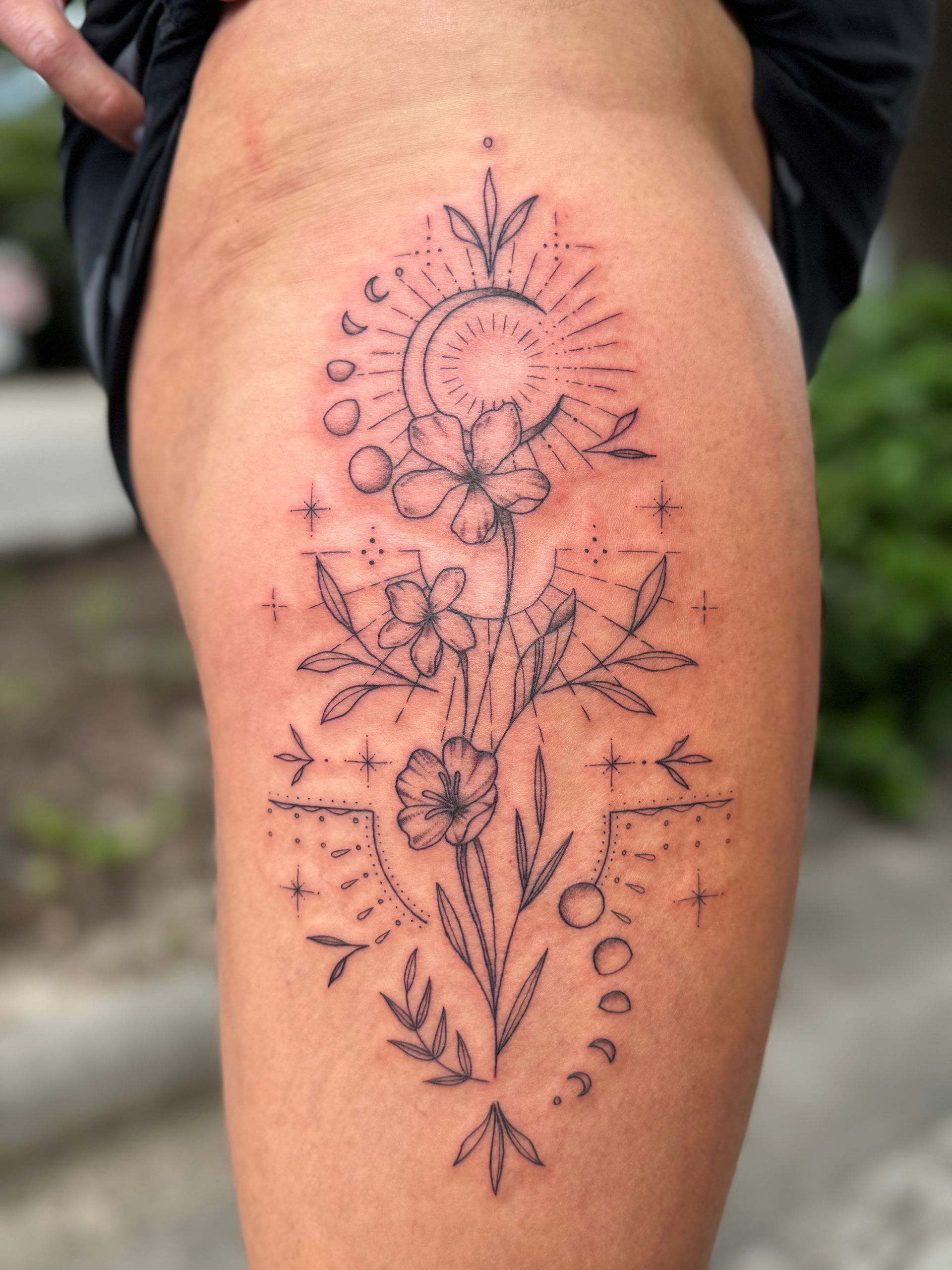 Floral line-art tattoo with a sunburst and dotted accents on a person’s upper thigh
