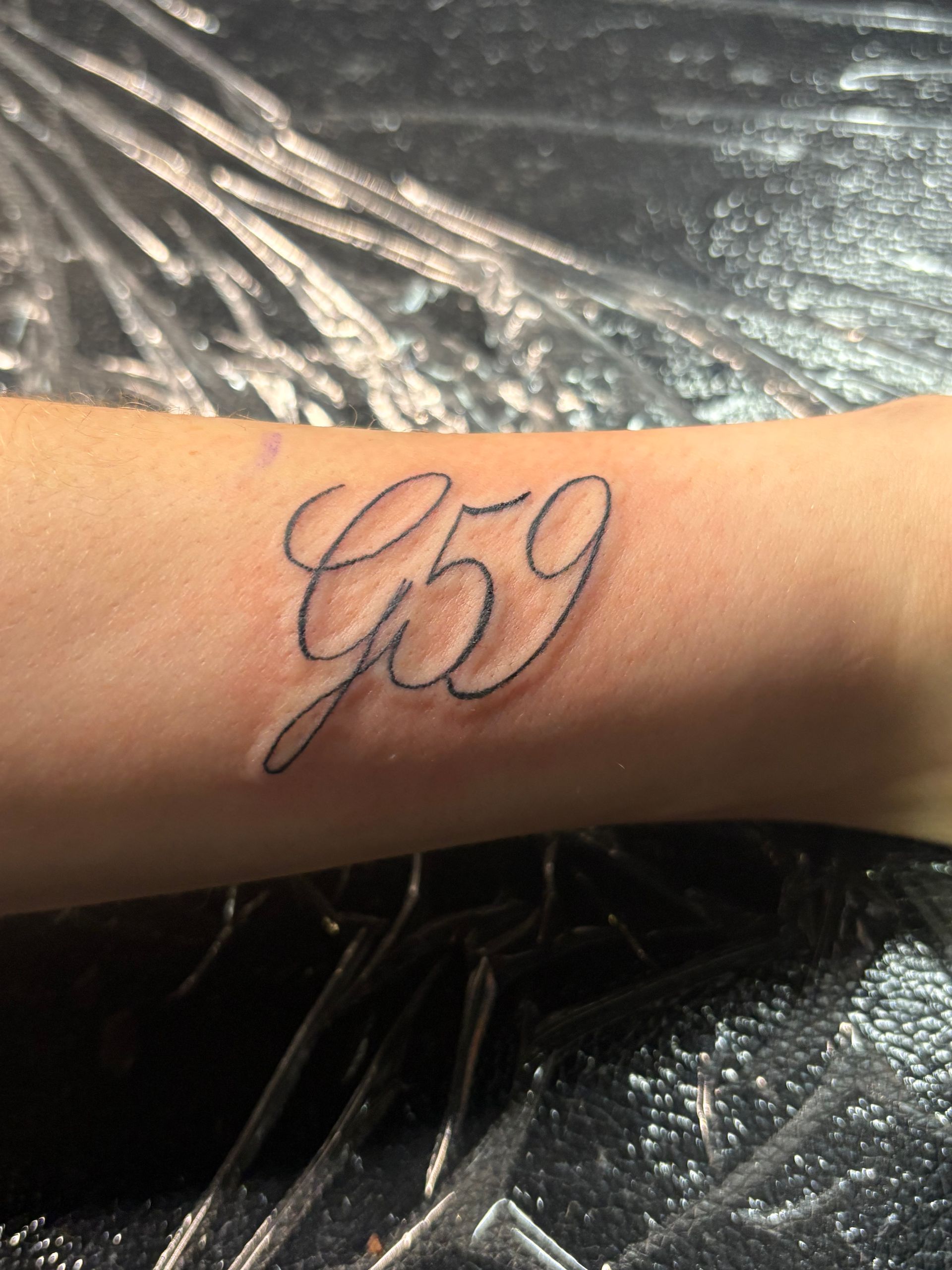 Close-up of a wrist with a cursive black tattoo reading “G9” on tan skin.