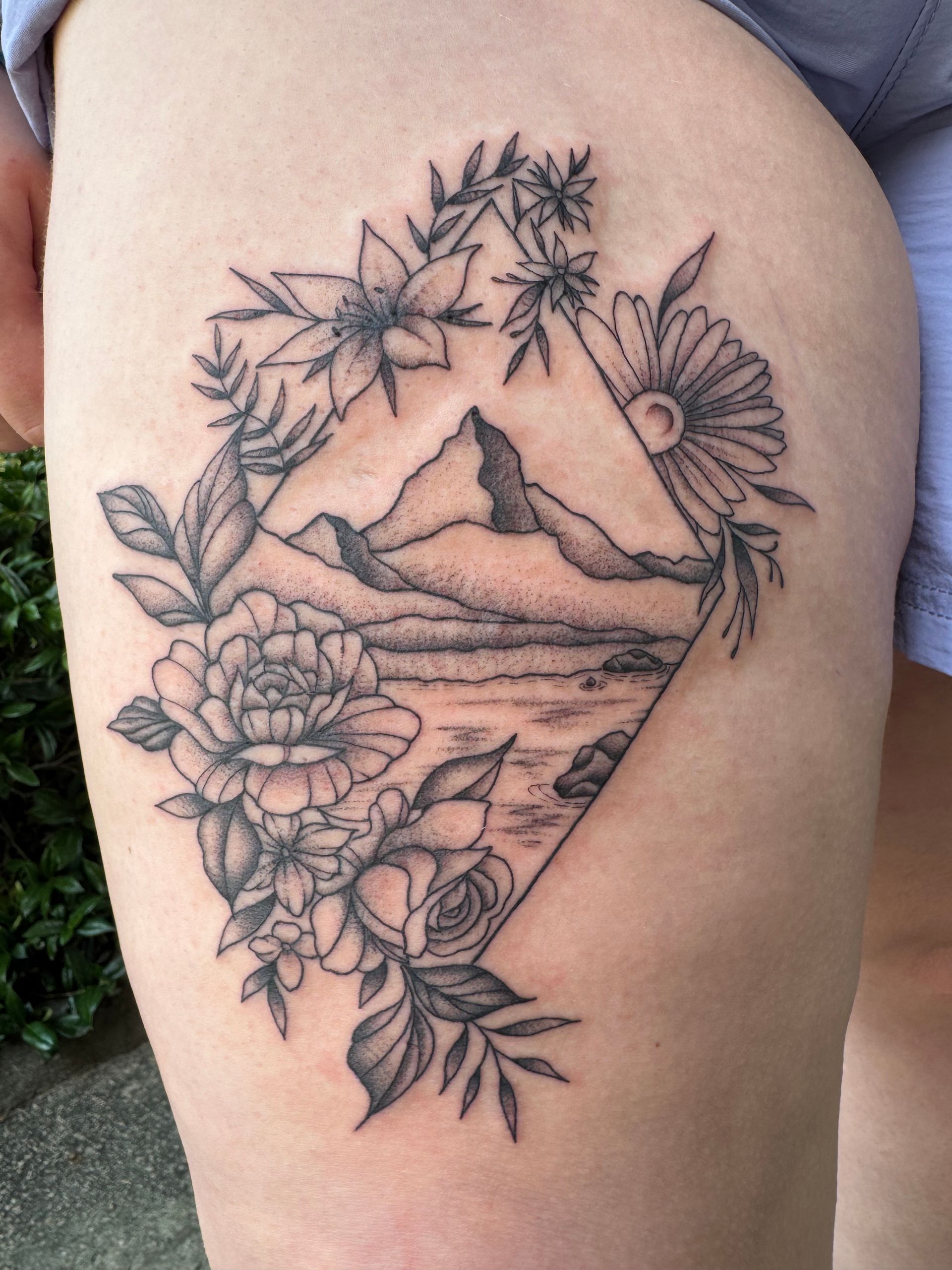 Black linework tattoo of a mountain landscape with flowers and leaves on skin