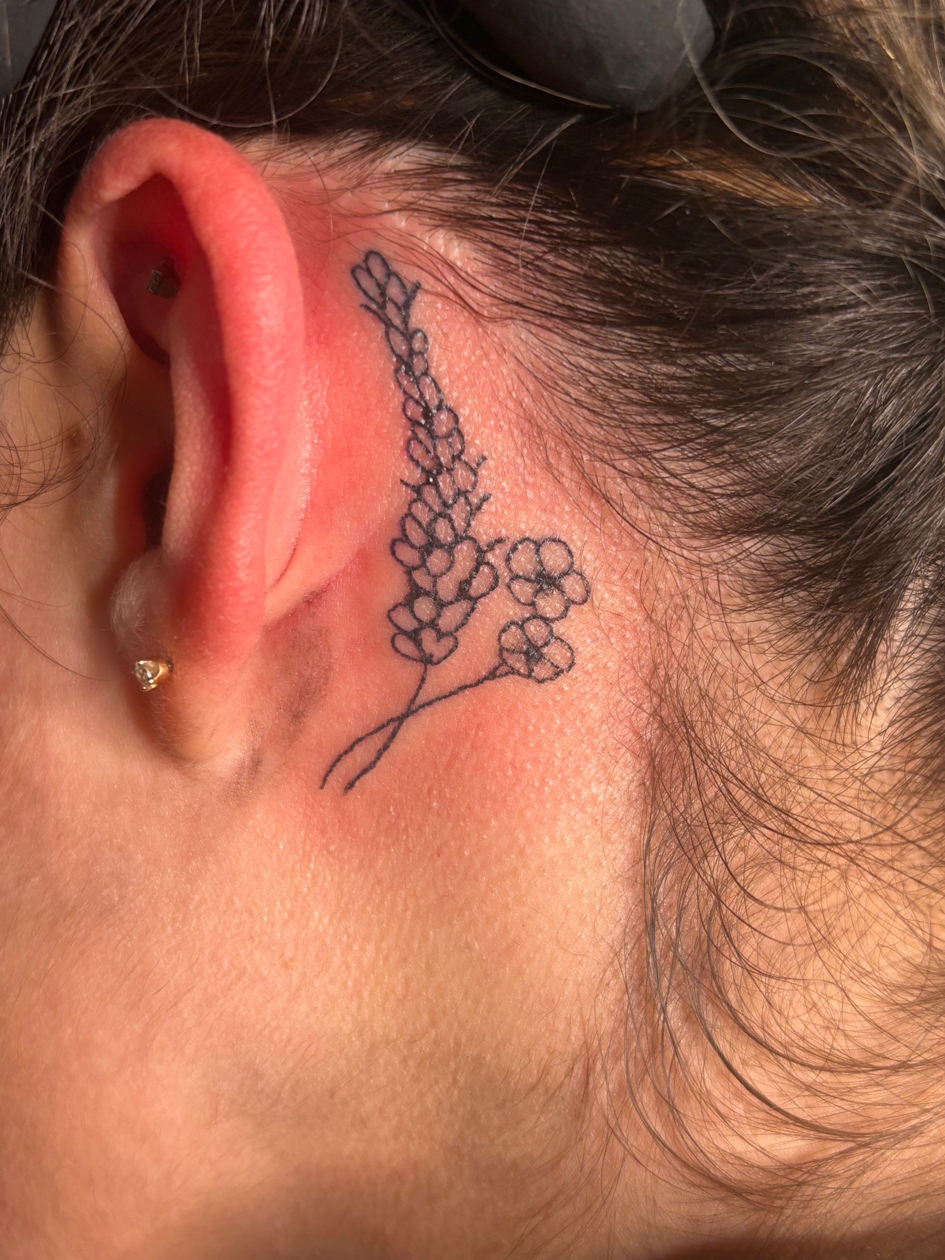 Small black floral tattoo behind an ear on skin with hair pulled back